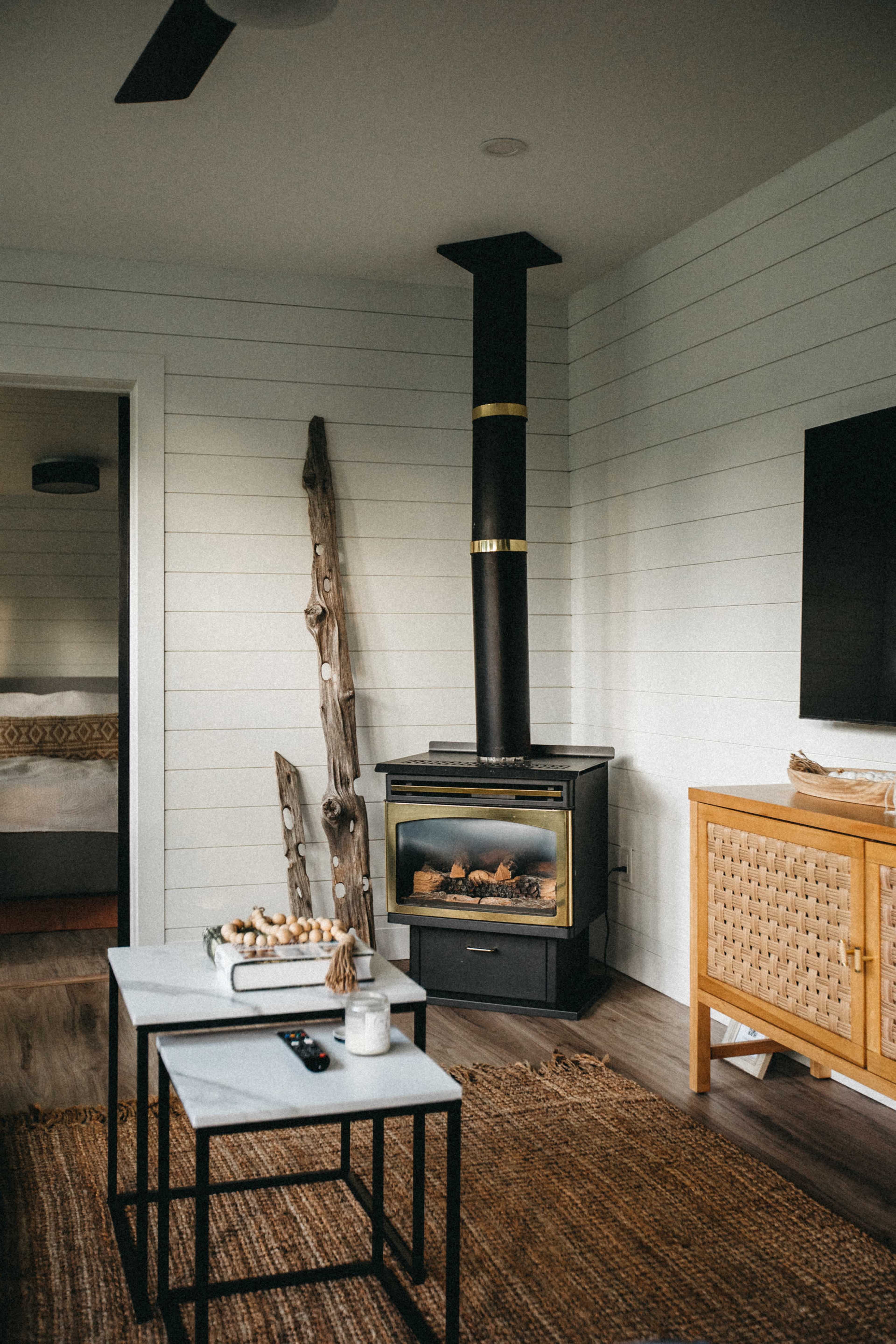 A living room features a black wood stove, a light-colored wooden coffee table, and woven decor accents on the floor.