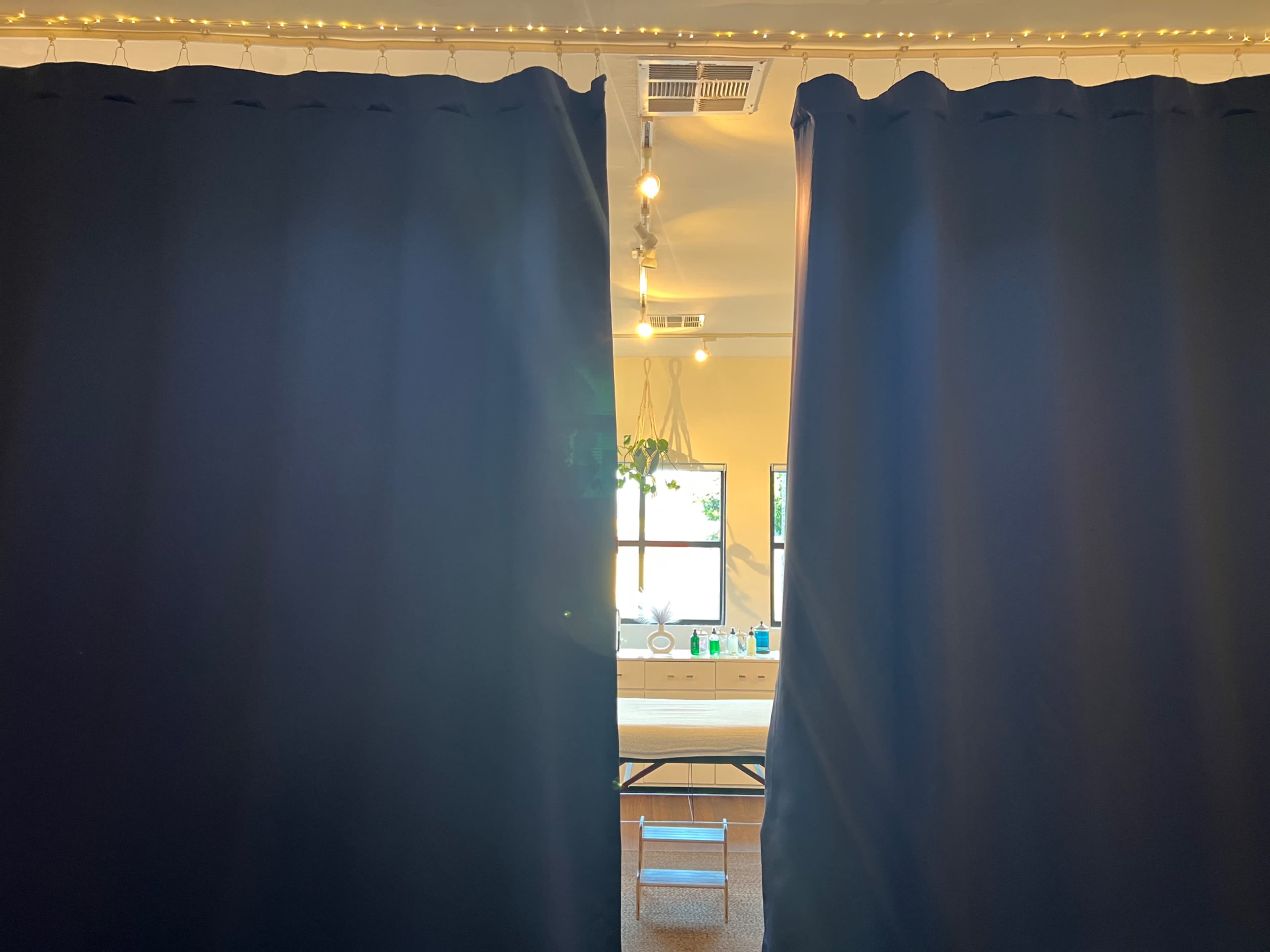 A pair of dark curtains partially opened reveals a well-lit room with a table and decorative plants.