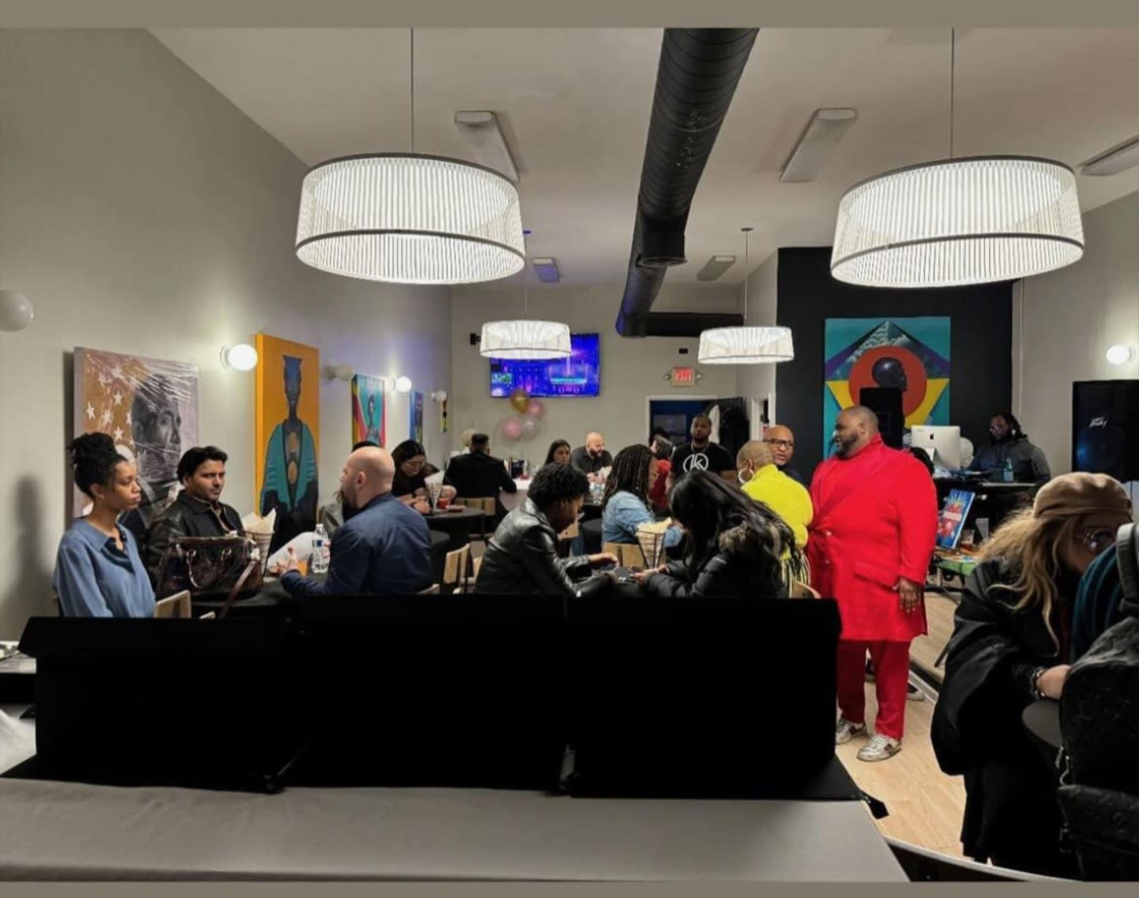 A diverse group of people socializes in a modern venue decorated with colorful artwork and pendant lighting.