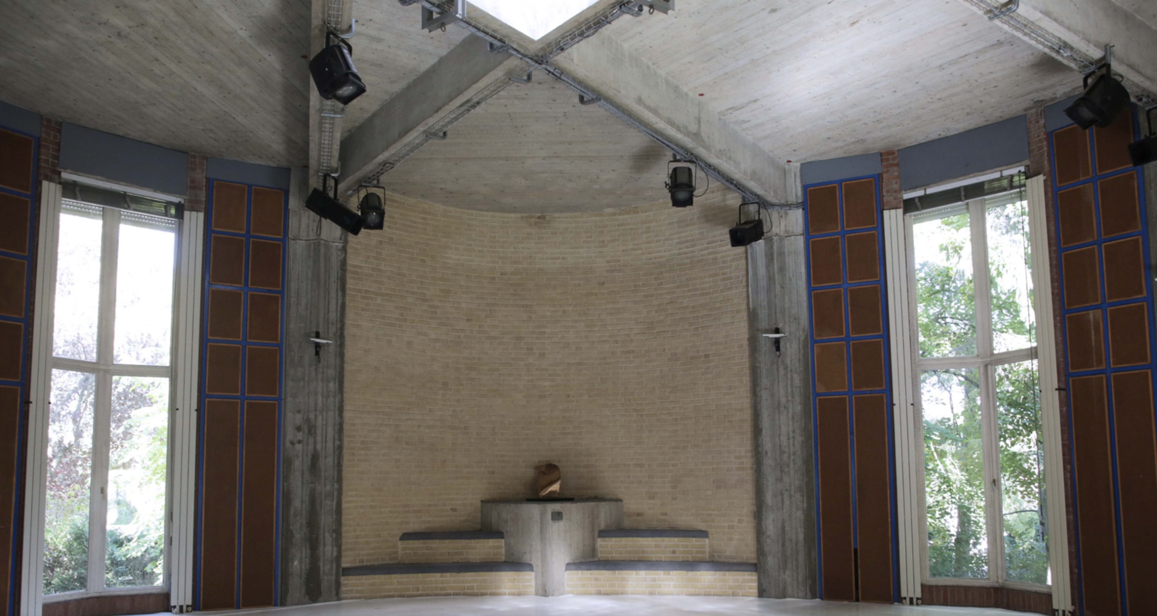 A simple, modern interior space with a rounded concrete ceiling, large windows, and minimal furnishings.