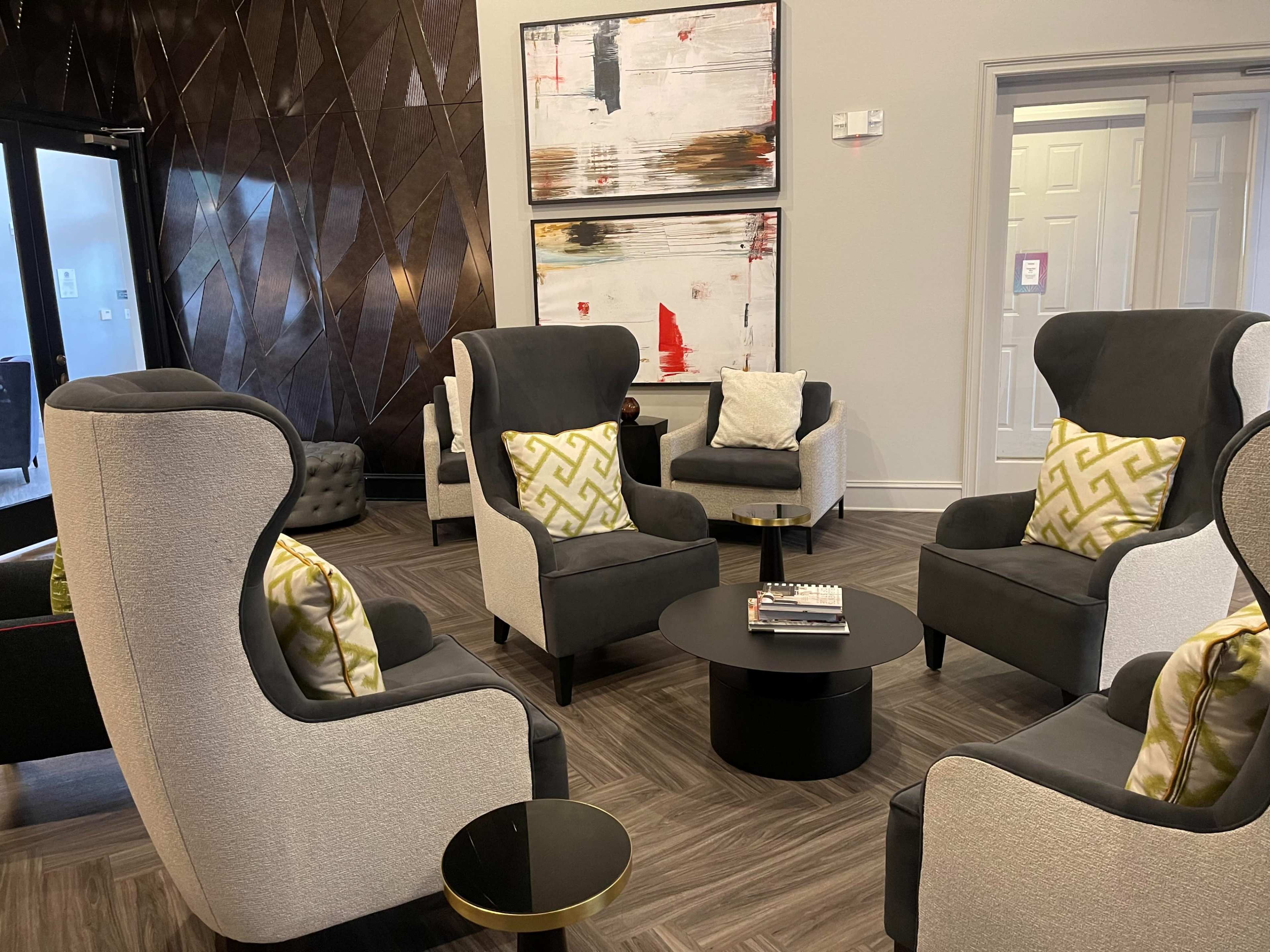 A modern lounge area featuring high-backed upholstered chairs with decorative pillows, a low black coffee table, and abstract artwork on the walls.