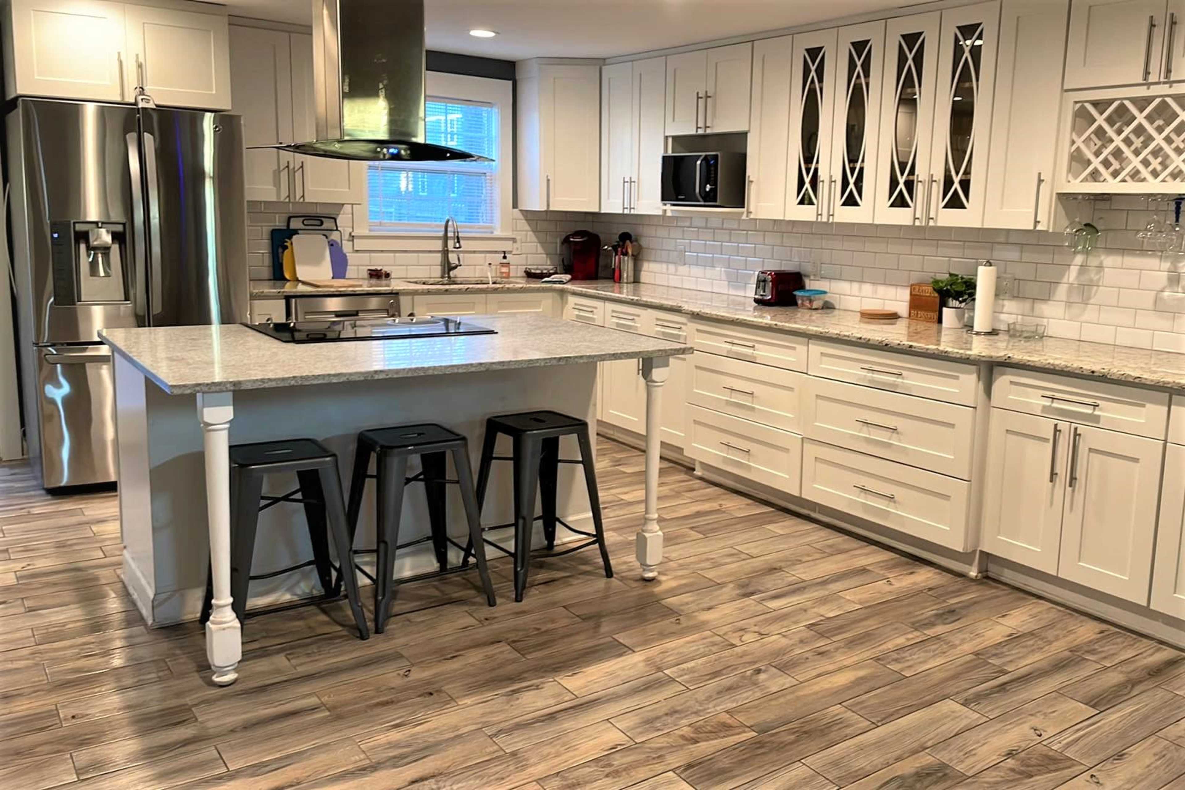 A modern kitchen featuring white cabinetry, a large gray countertop island with three black stools, and stainless steel appliances.