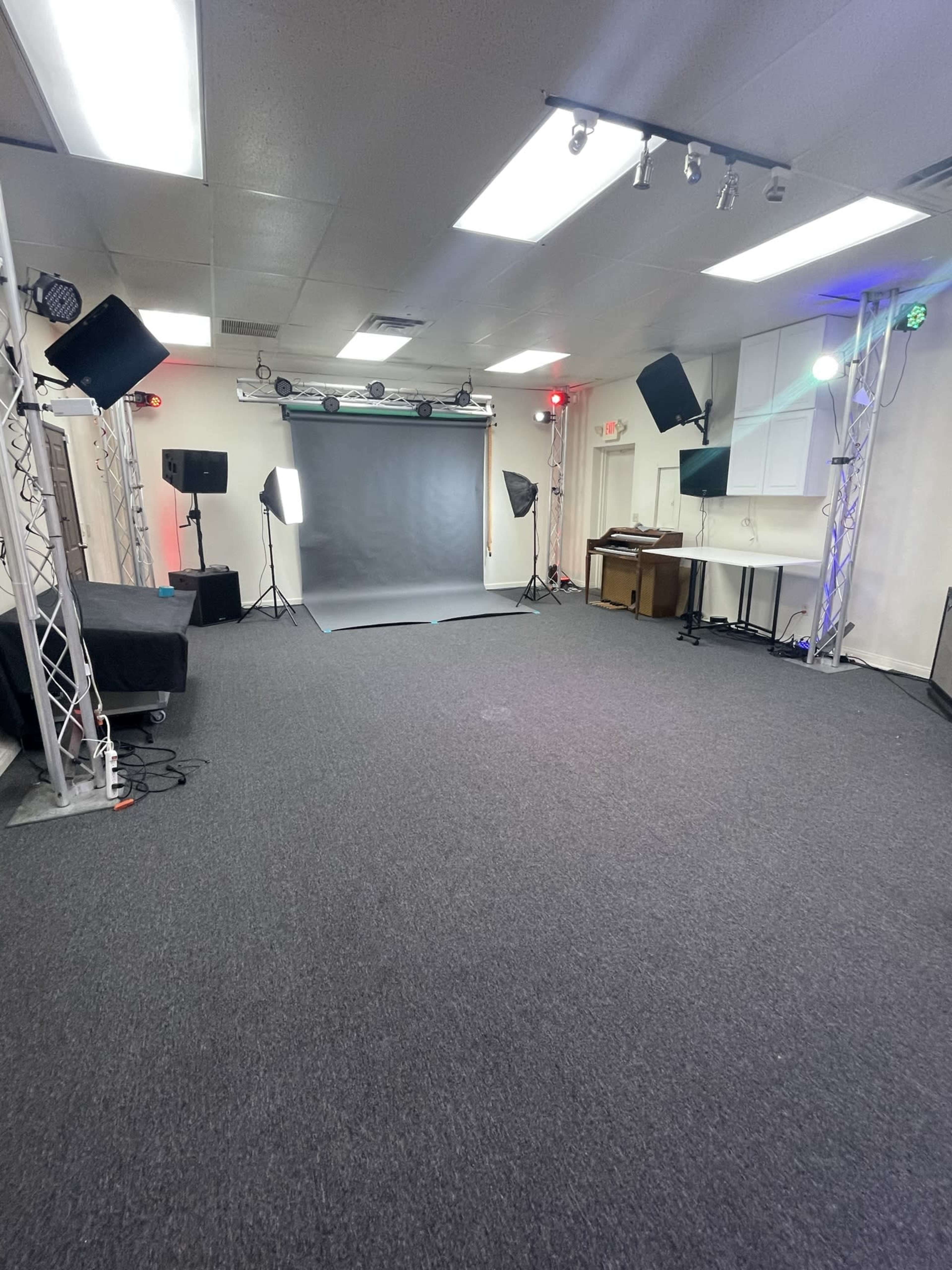 A well-lit studio space with a gray backdrop, studio lights, and sound equipment arranged on a carpeted floor.