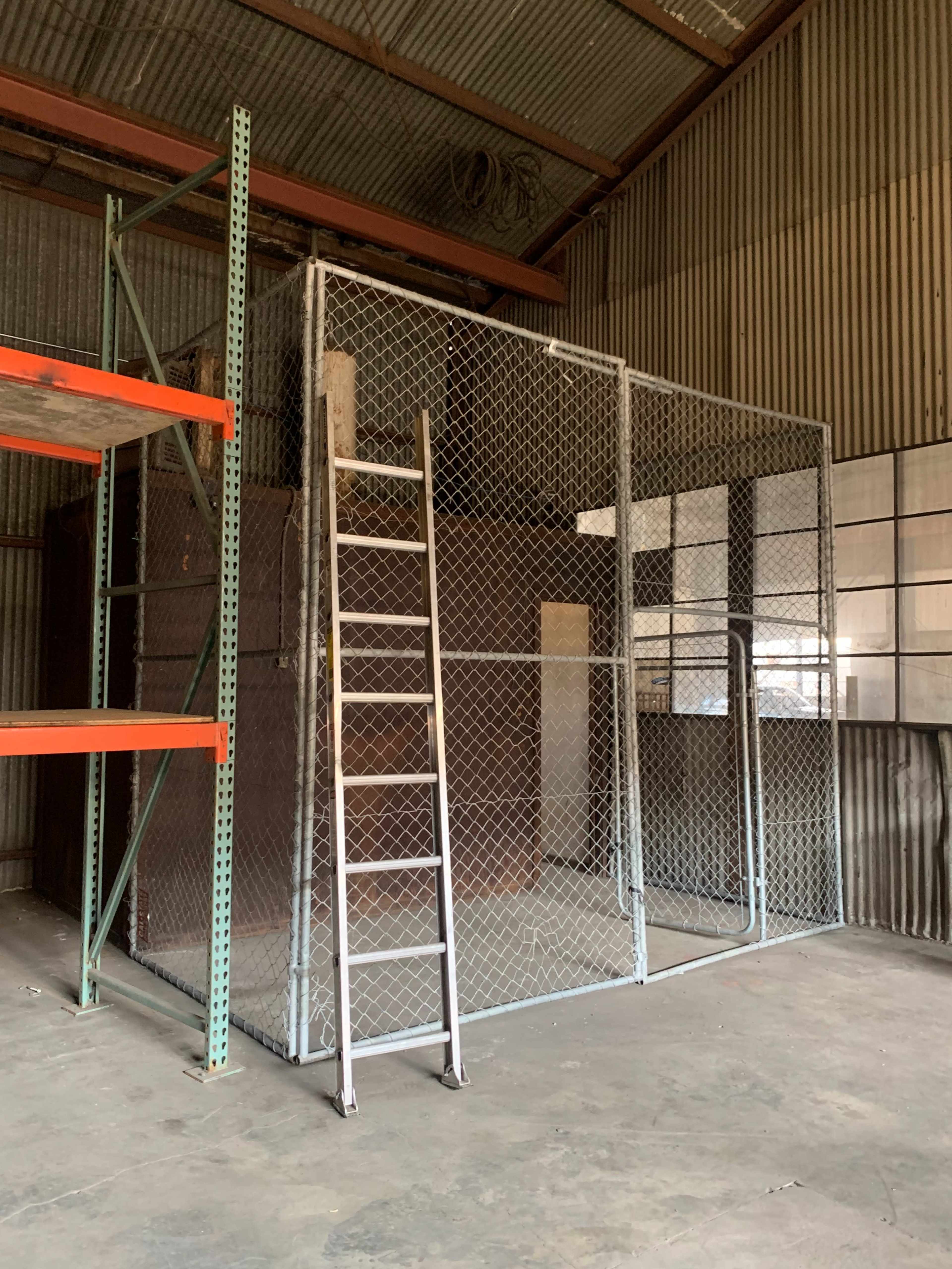 A wire mesh storage cage within a warehouse, accompanied by a metal ladder leaning against it.