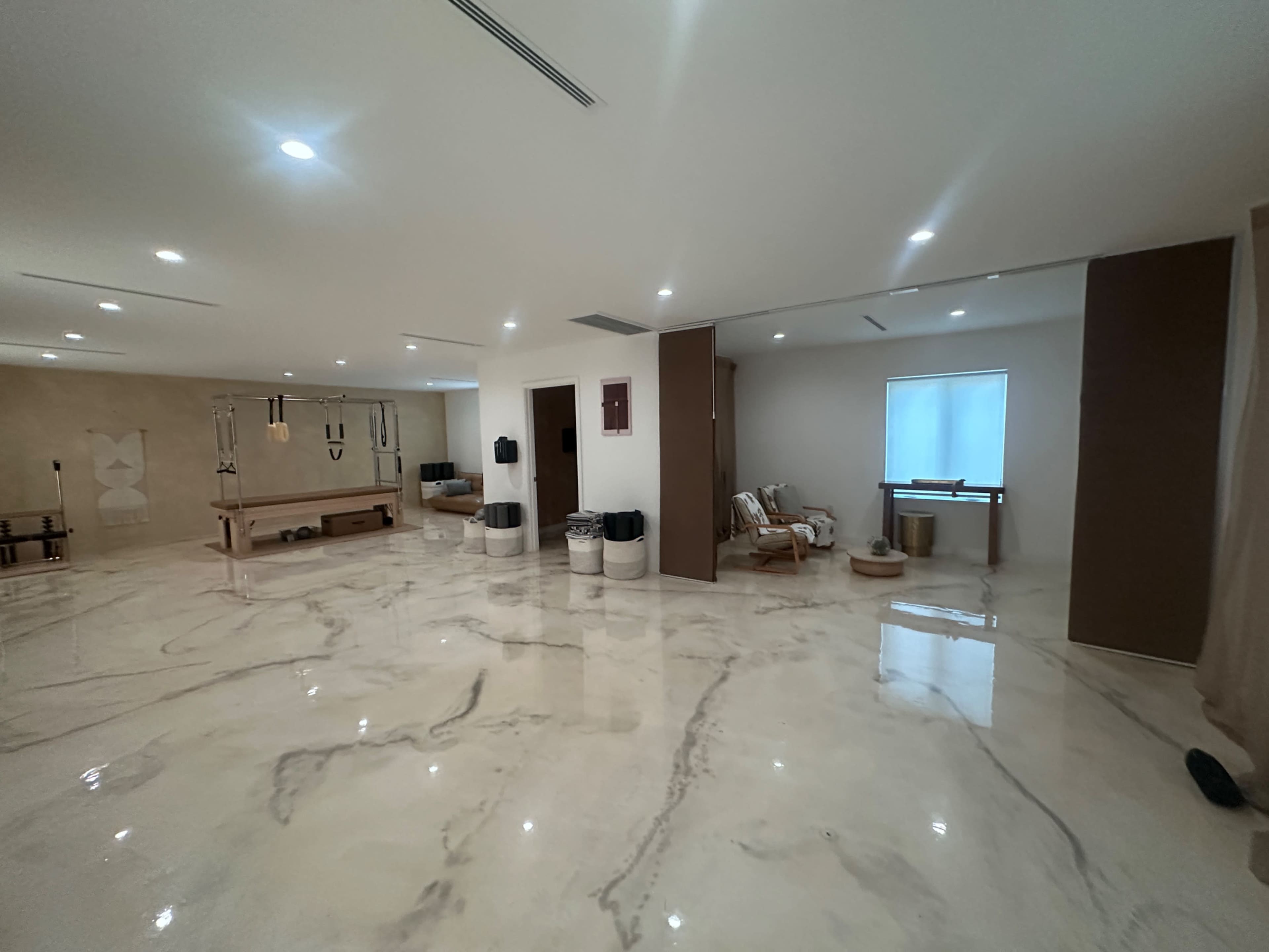 The image shows a spacious interior room with polished marble flooring, various modern furnishings, and ample natural light coming through a window.