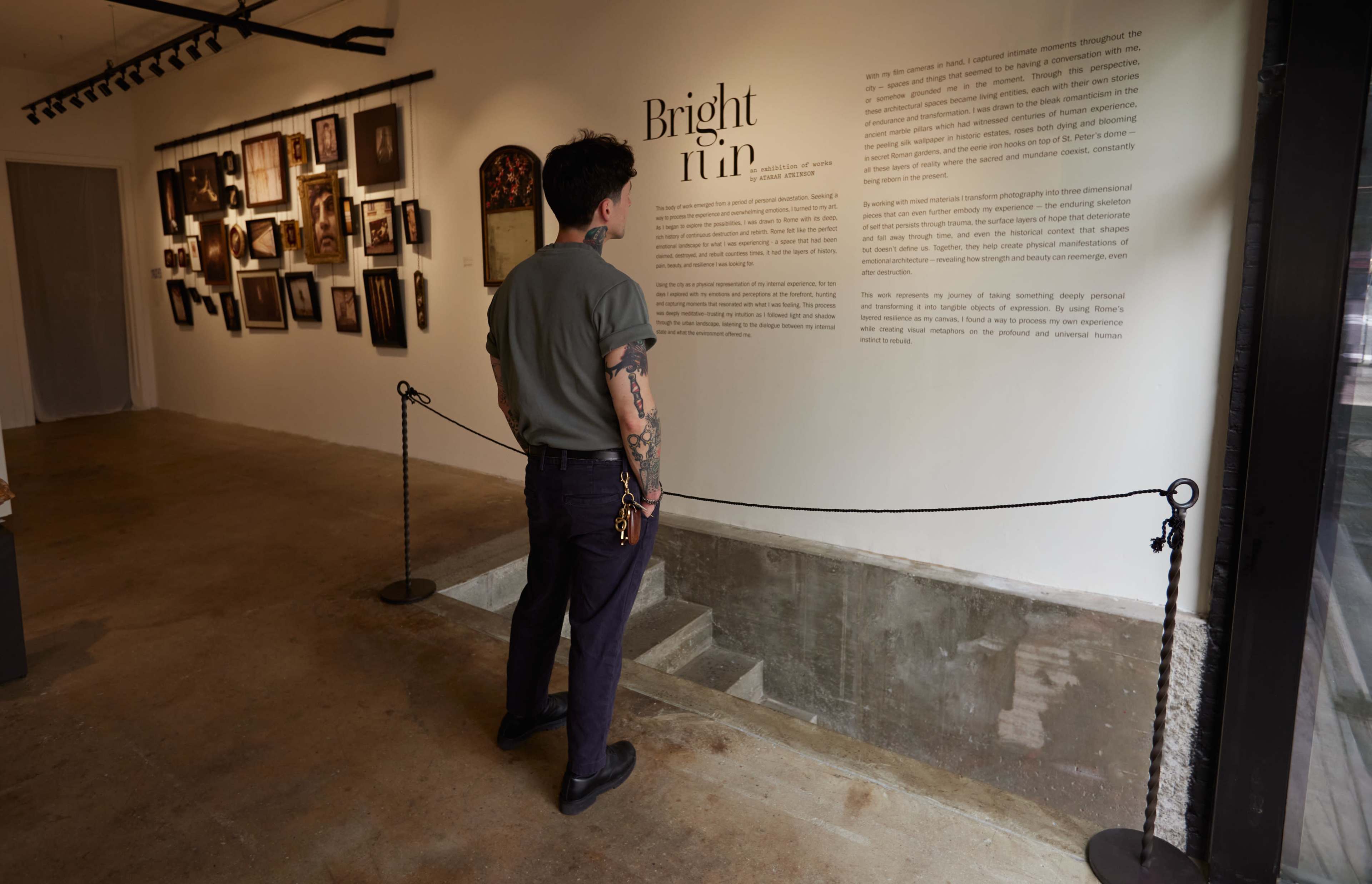 A person stands in an art gallery, reading an informational display titled "Bright Turn" on the wall, surrounded by framed photographs and artworks.