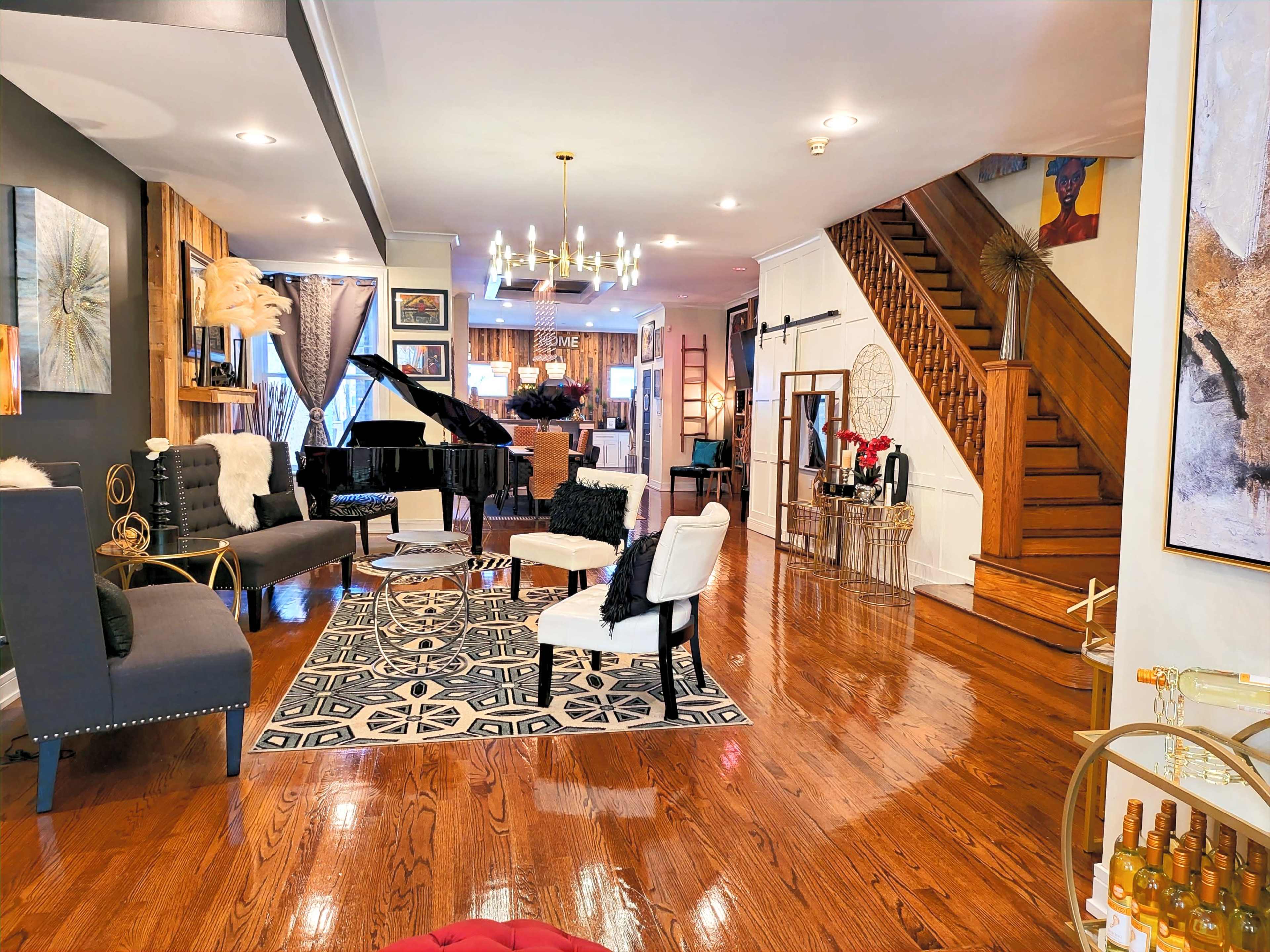 A stylish living room with hardwood floors, a grand piano, seating arrangements, and a staircase leading to an upper level.