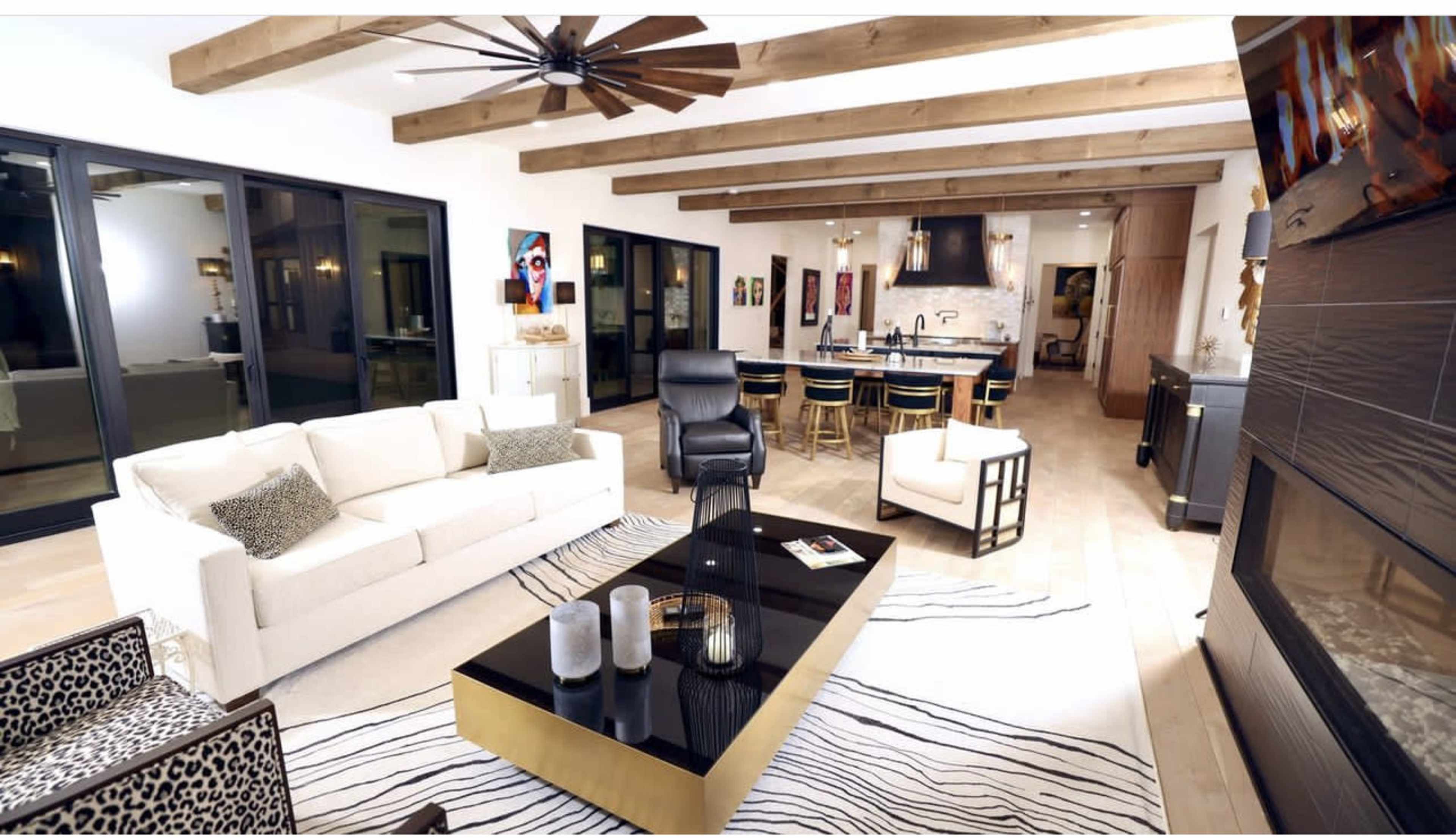 A spacious living room featuring a white sofa, a black coffee table, and a dining area with wooden beams and large windows.