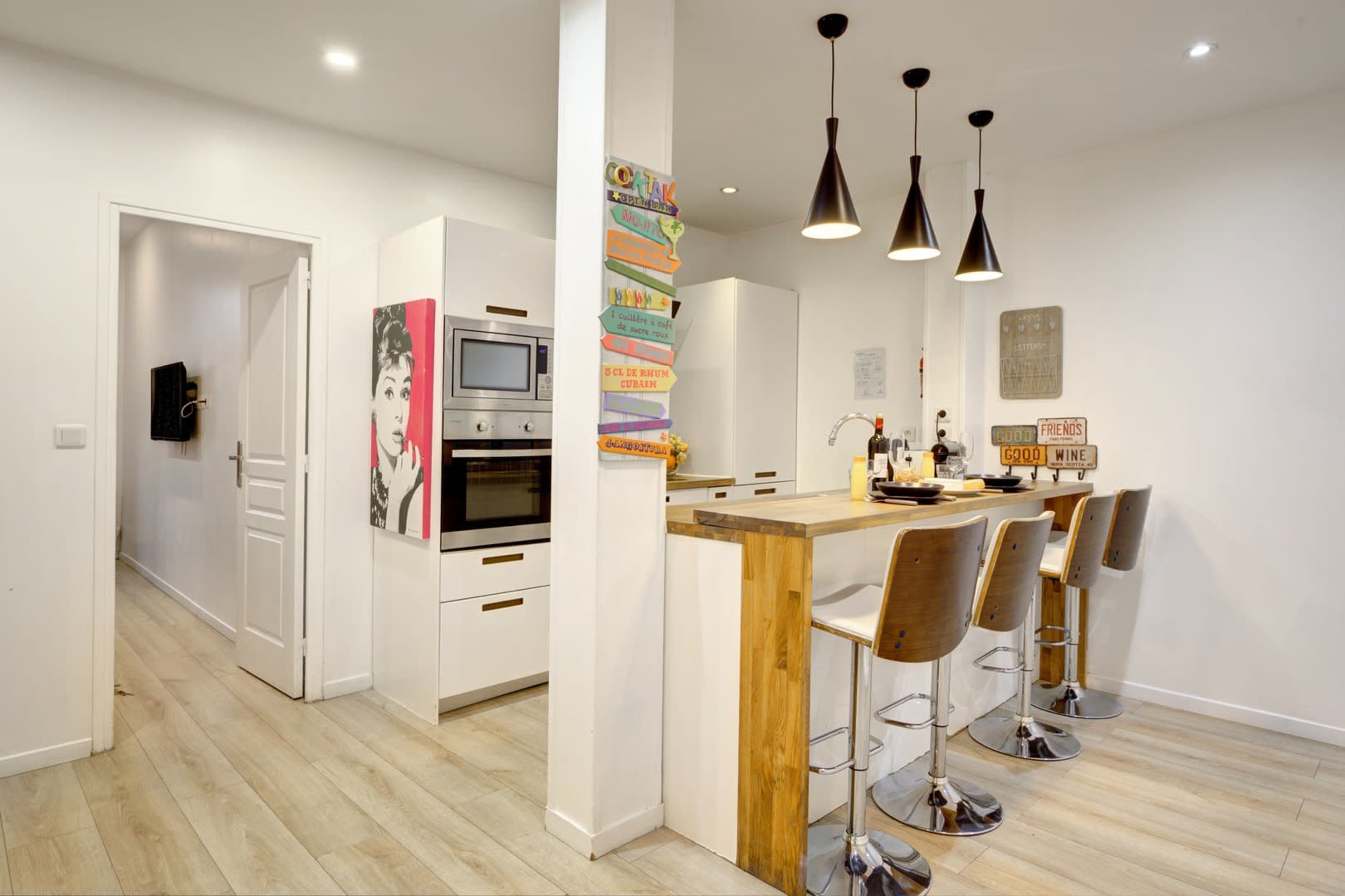 A modern kitchen features a wooden island with bar stools, white cabinetry, and pendant lighting.