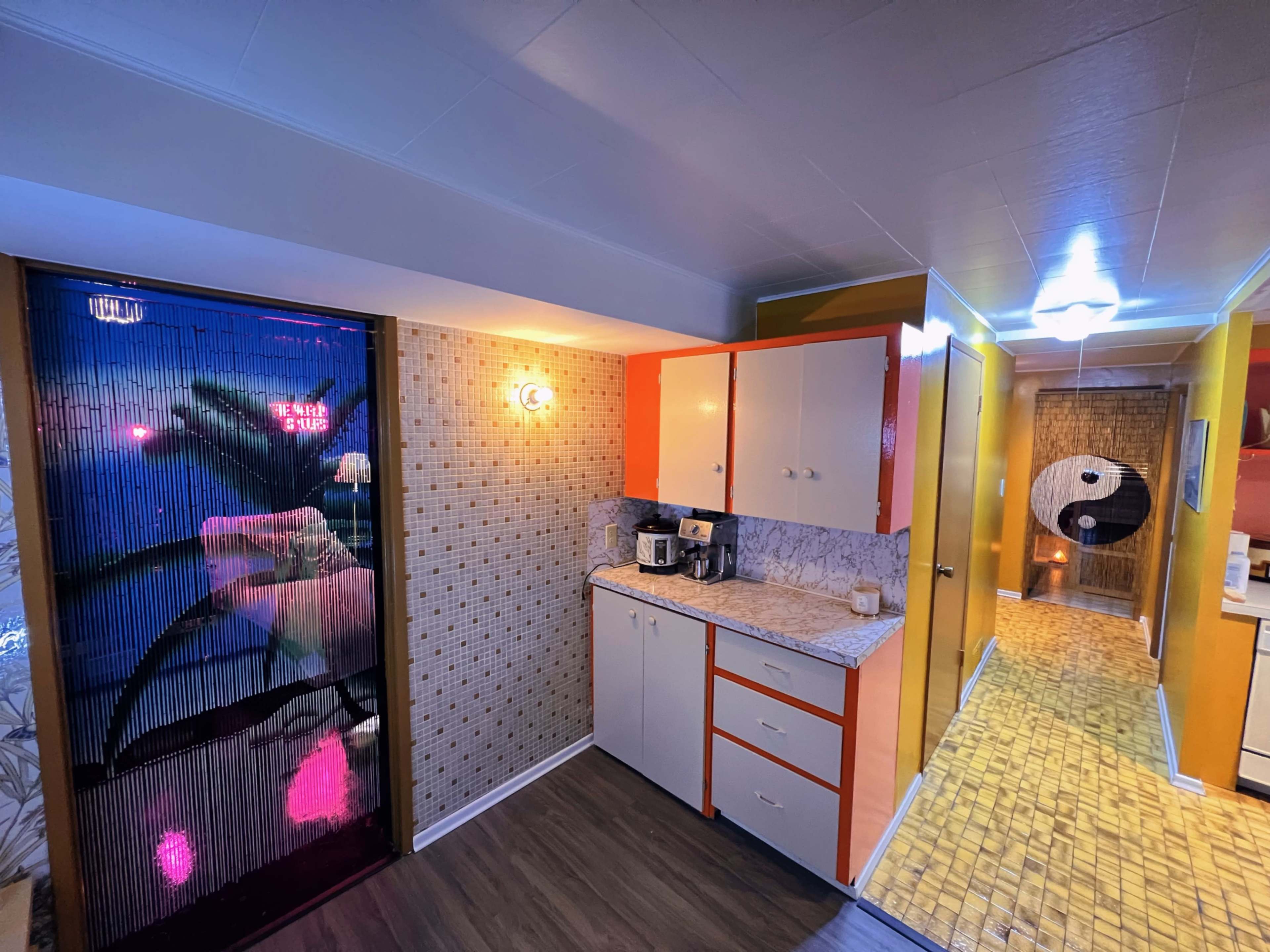 A brightly colored hallway leading to a kitchen area, featuring a floral curtain, a countertop with kitchen appliances, and a wall adorned with a yin-yang symbol.
