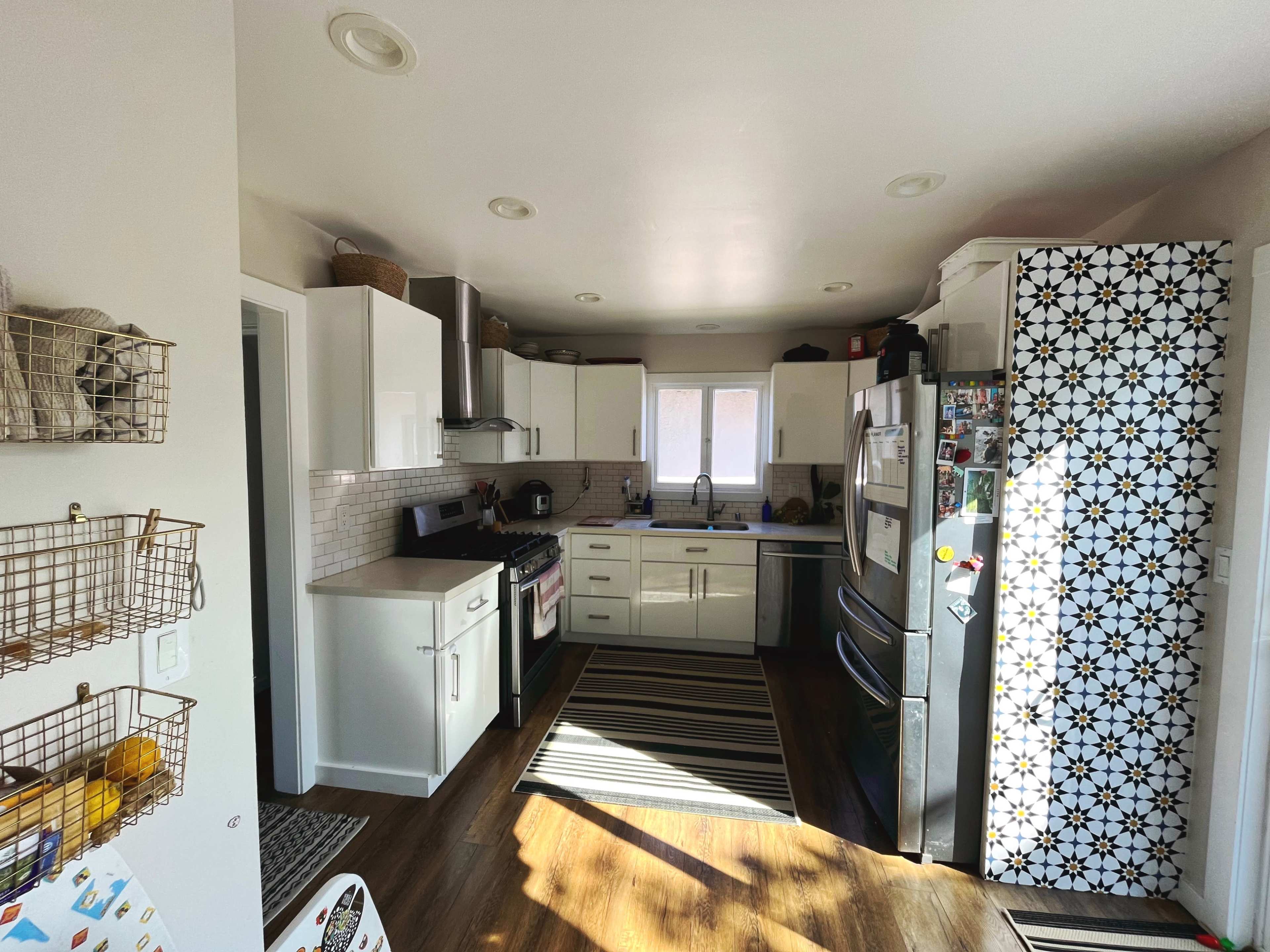 A bright kitchen features white cabinets, a stainless steel refrigerator, and a striped rug on the floor.