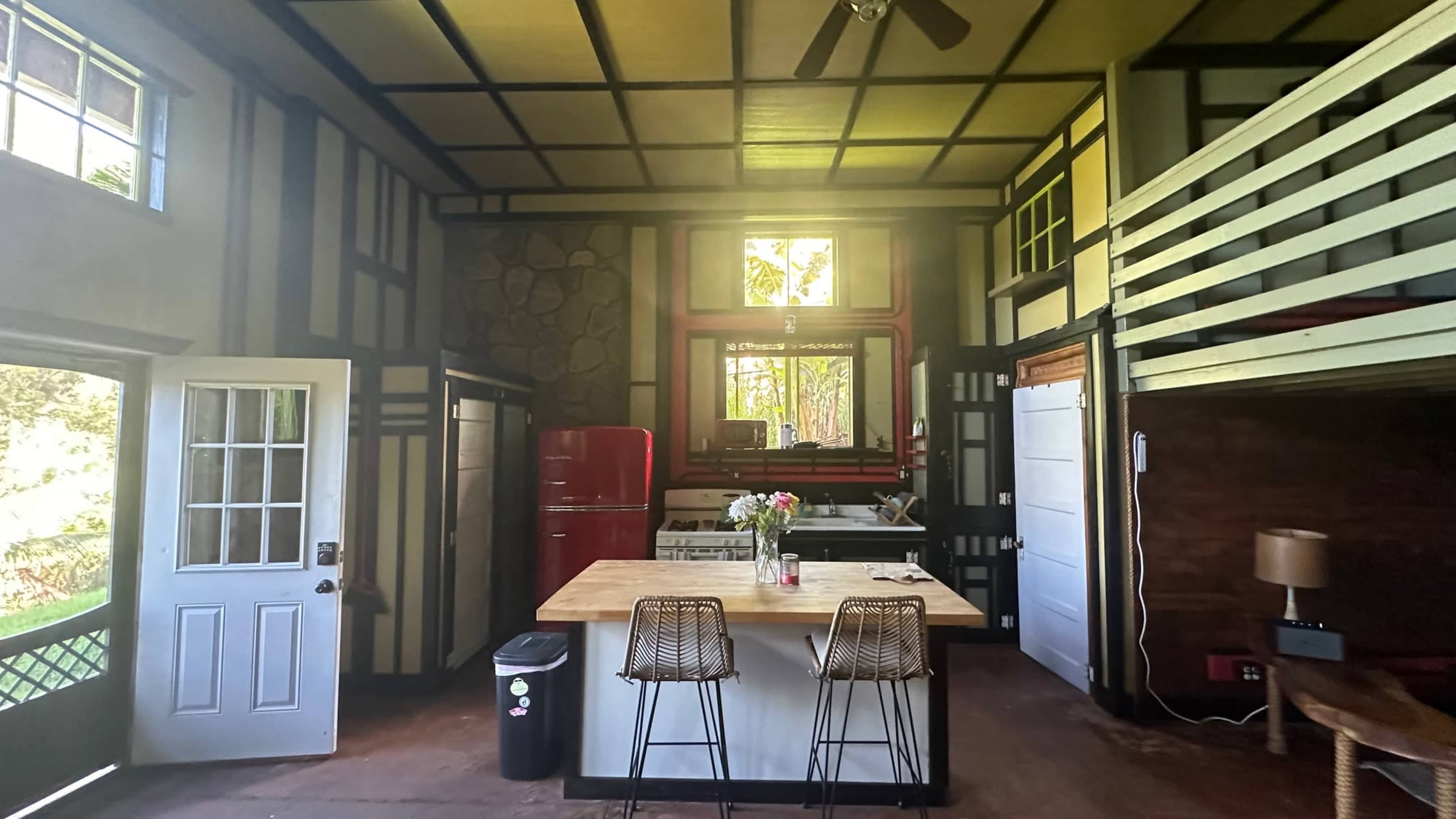 A spacious, modern kitchen and living area with a lofted sleeping area, featuring a red refrigerator and a large island with bar stools.