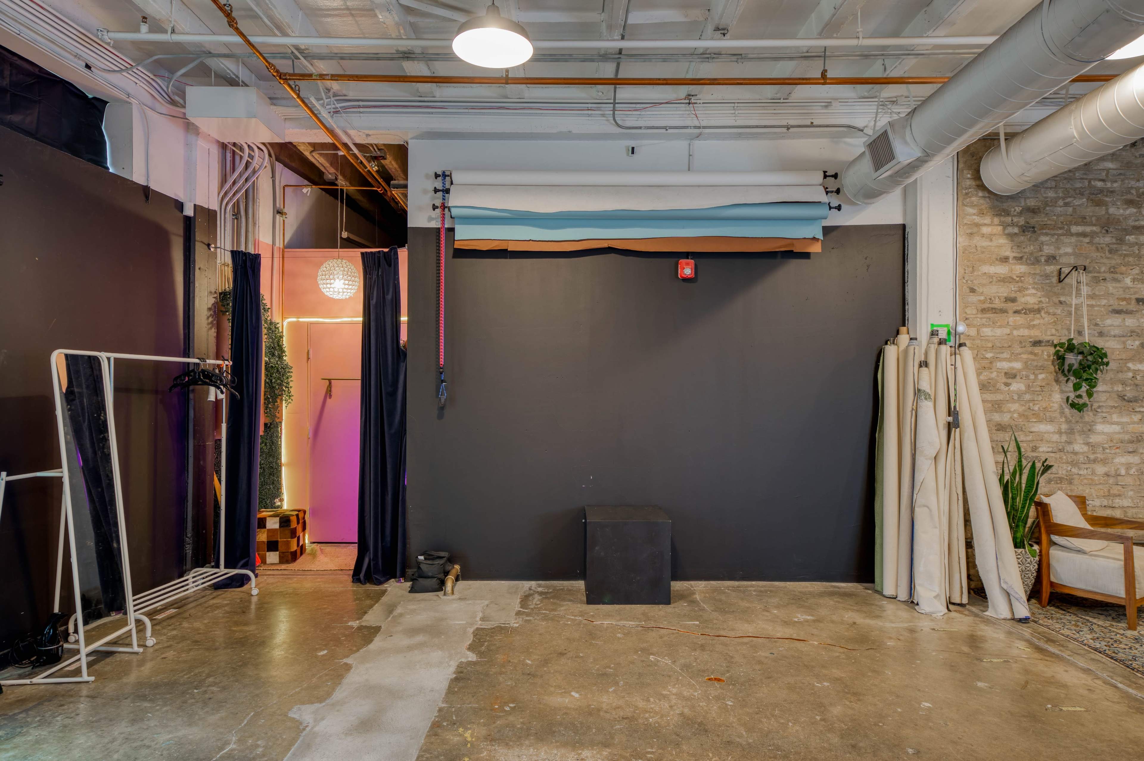 A spacious studio with exposed brick walls, a concrete floor, and a black backdrop, along with various props and curtains.