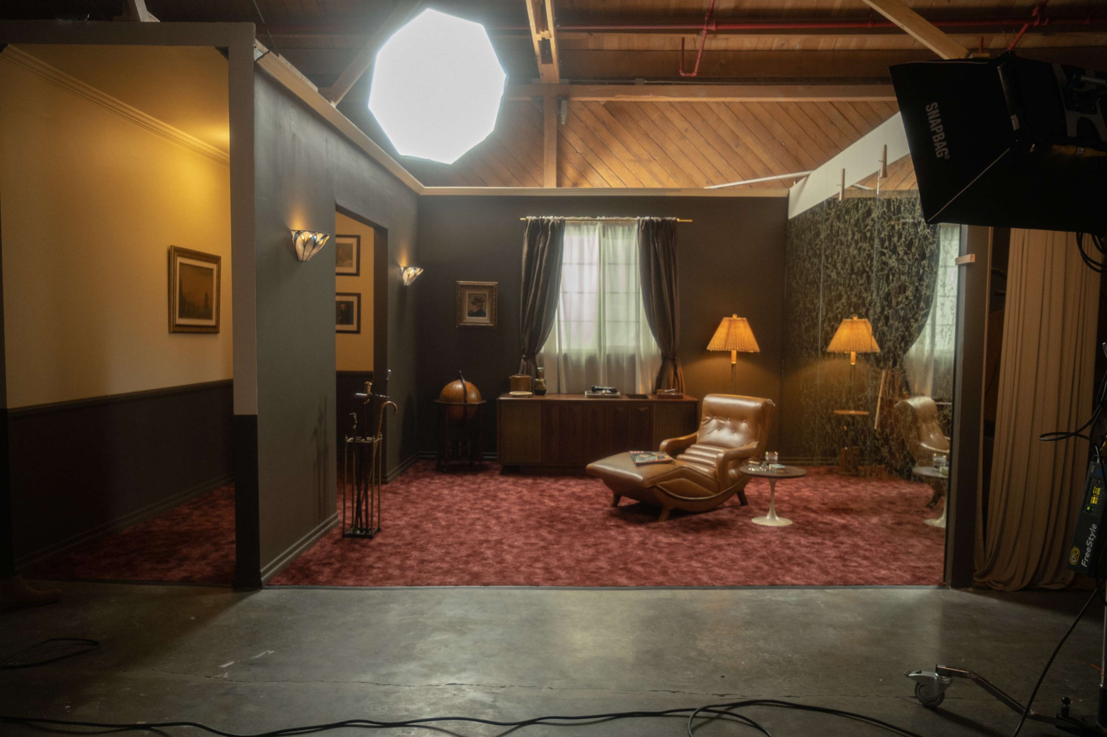 A well-lit, staged room featuring a brown leather lounge chair, two lamps, and vintage decor against a backdrop of grey and maroon walls.
