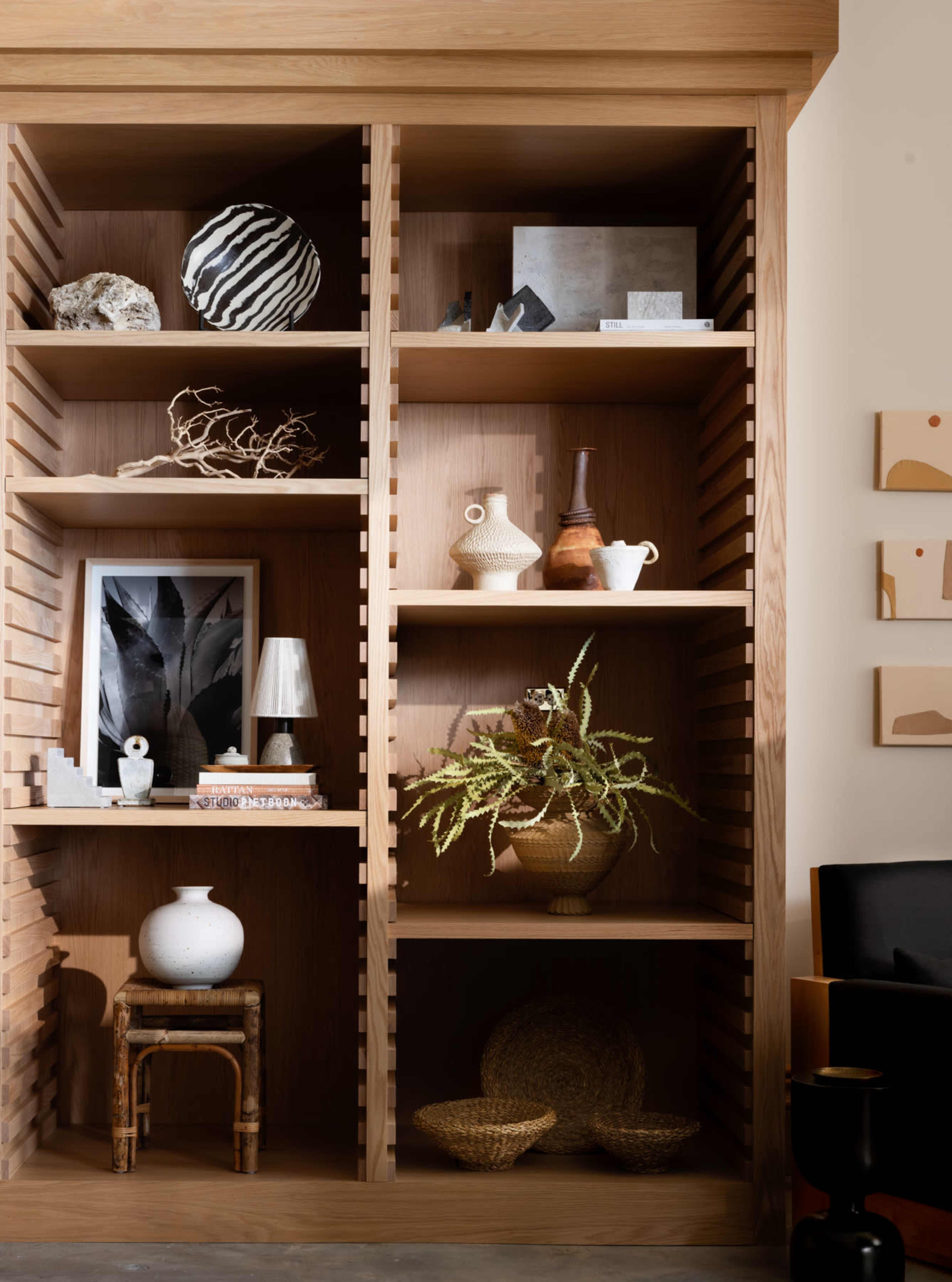 A wooden shelving unit filled with various decorative items, including vases, artwork, and houseplants.