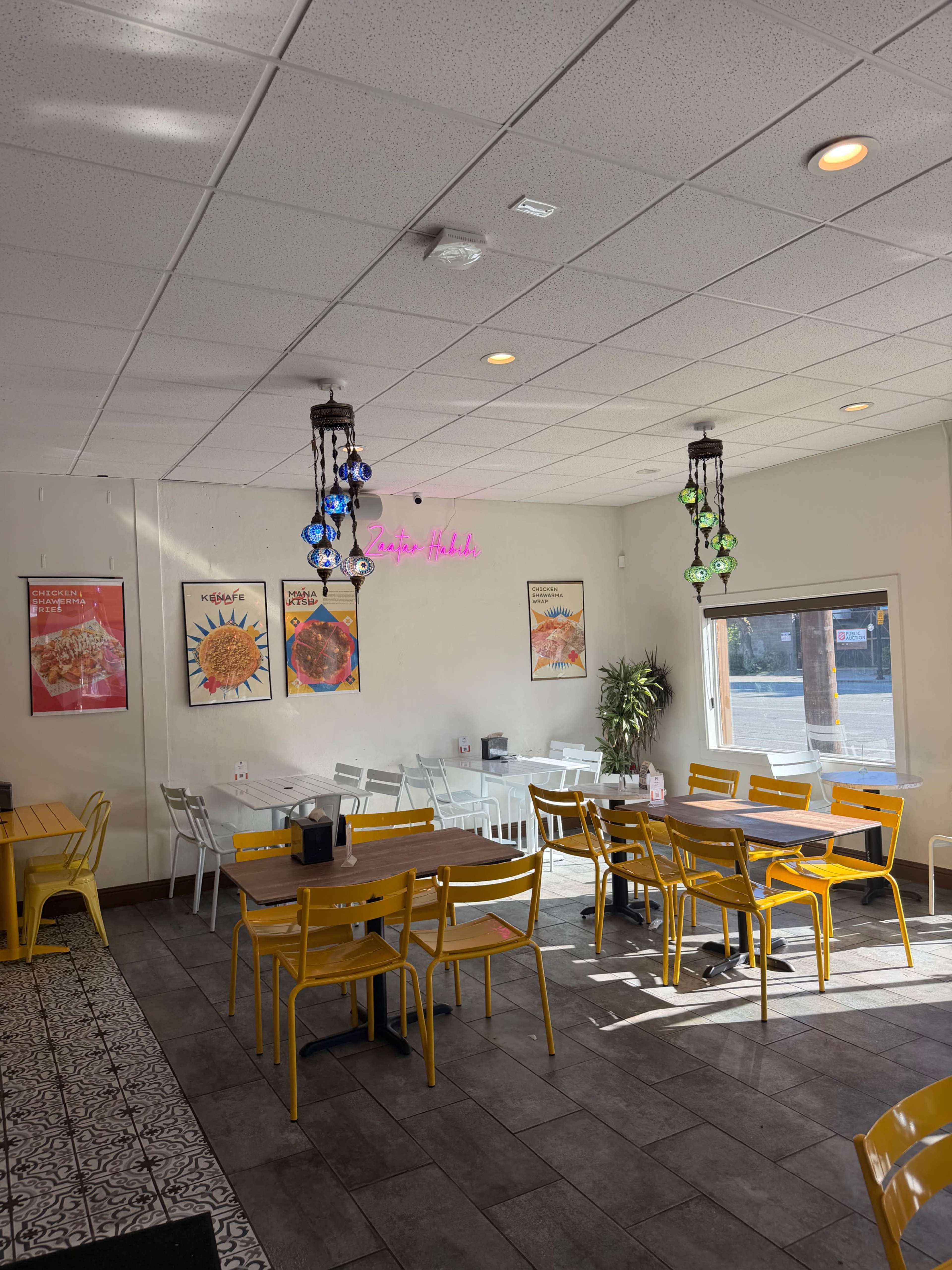 The interior of a casual dining restaurant features yellow chairs and tables, decorative posters on the walls, and colorful hanging lights.