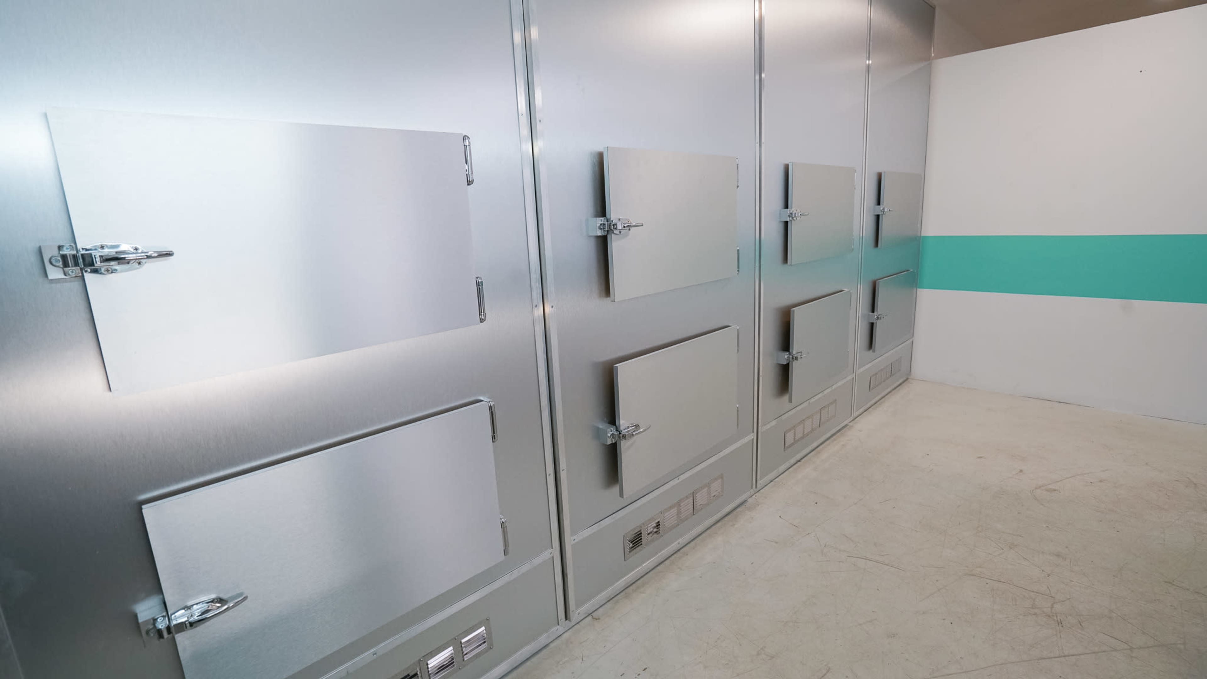 The image shows a sterile room with several metal storage compartments mounted on a wall, featuring small hinged doors.