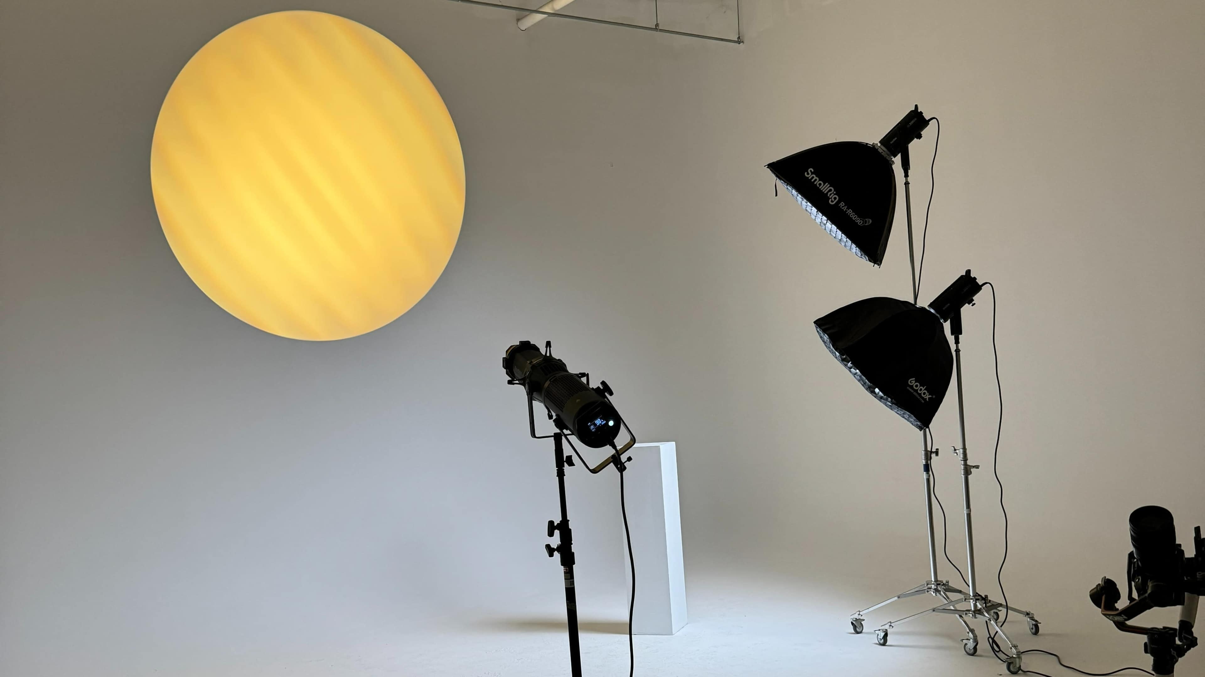 A photography studio with a large yellow circular backdrop and three lighting setups, including two softboxes and a spotlight.