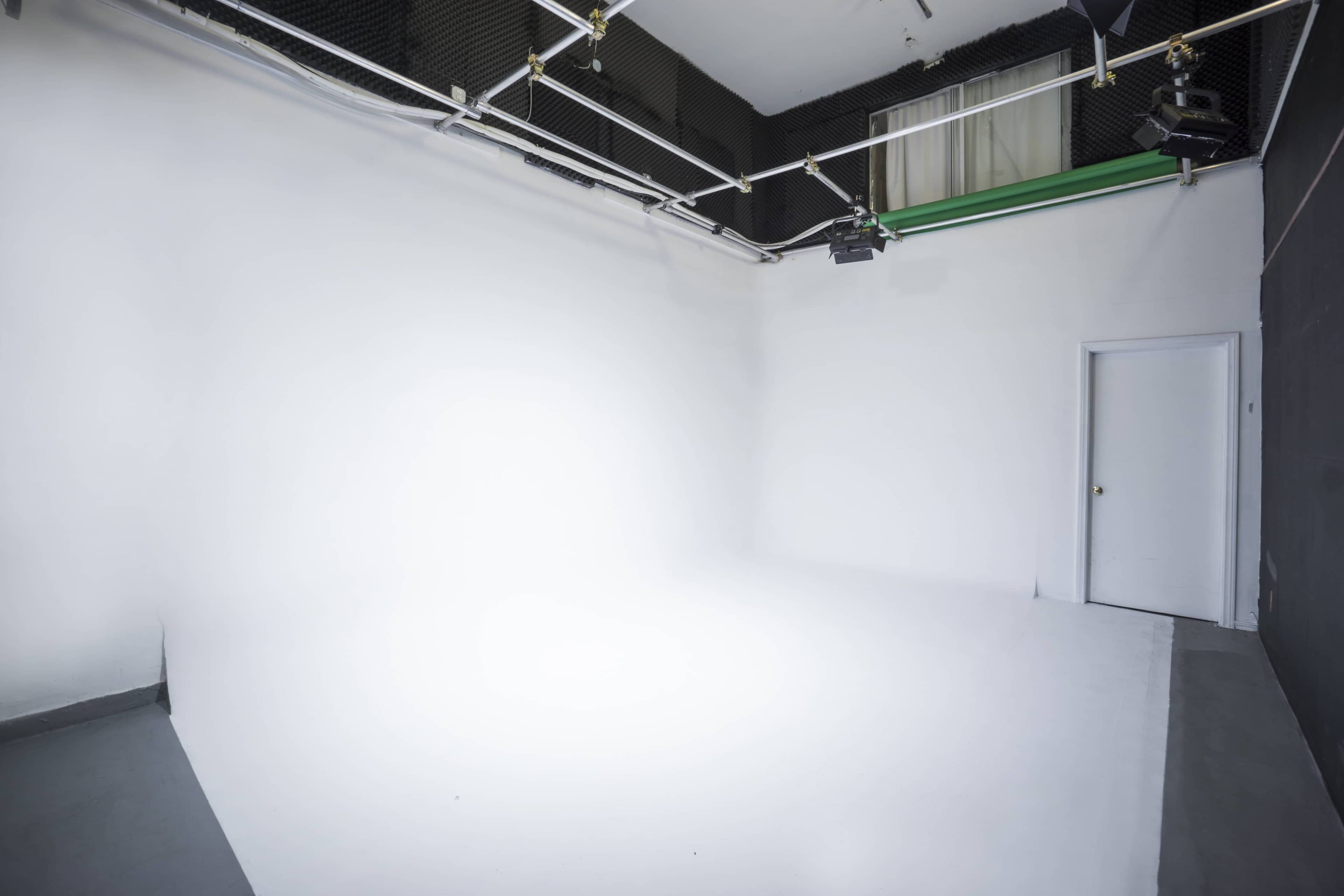 A large empty photo studio with white walls, a seamless backdrop, and a closed door.