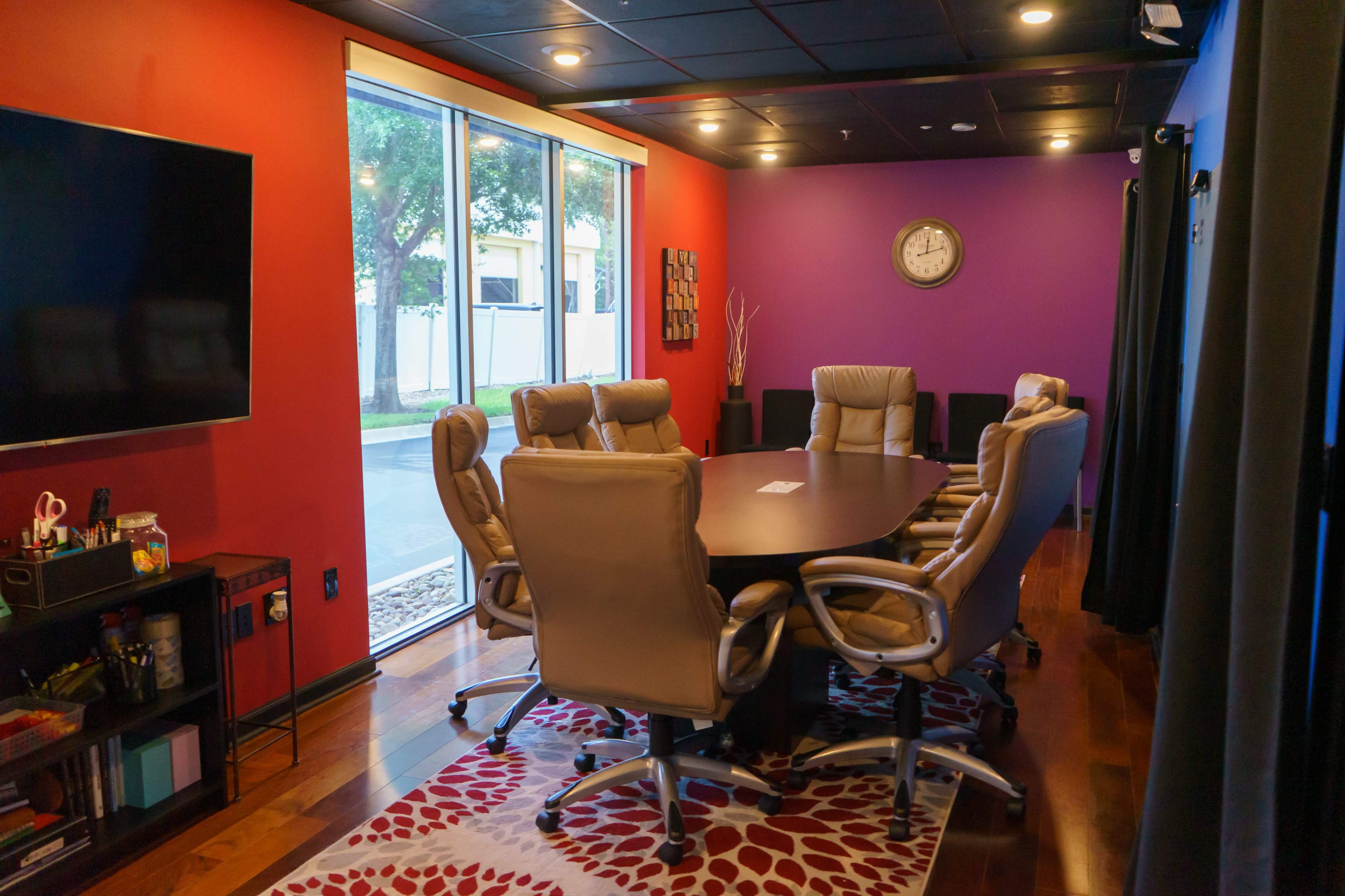 A conference room features a large table surrounded by ergonomic chairs, with colorful walls and large windows allowing natural light.
