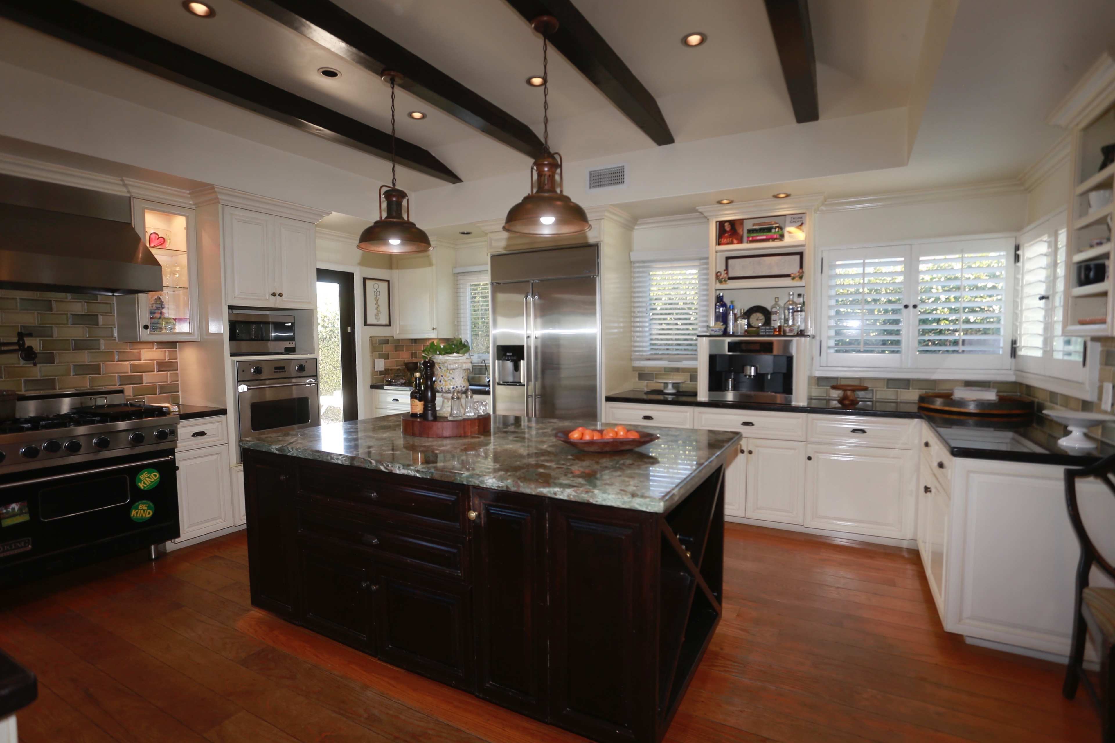 The kitchen features a central island with a dark wood base, stainless steel appliances, and white cabinetry with a tile backsplash.