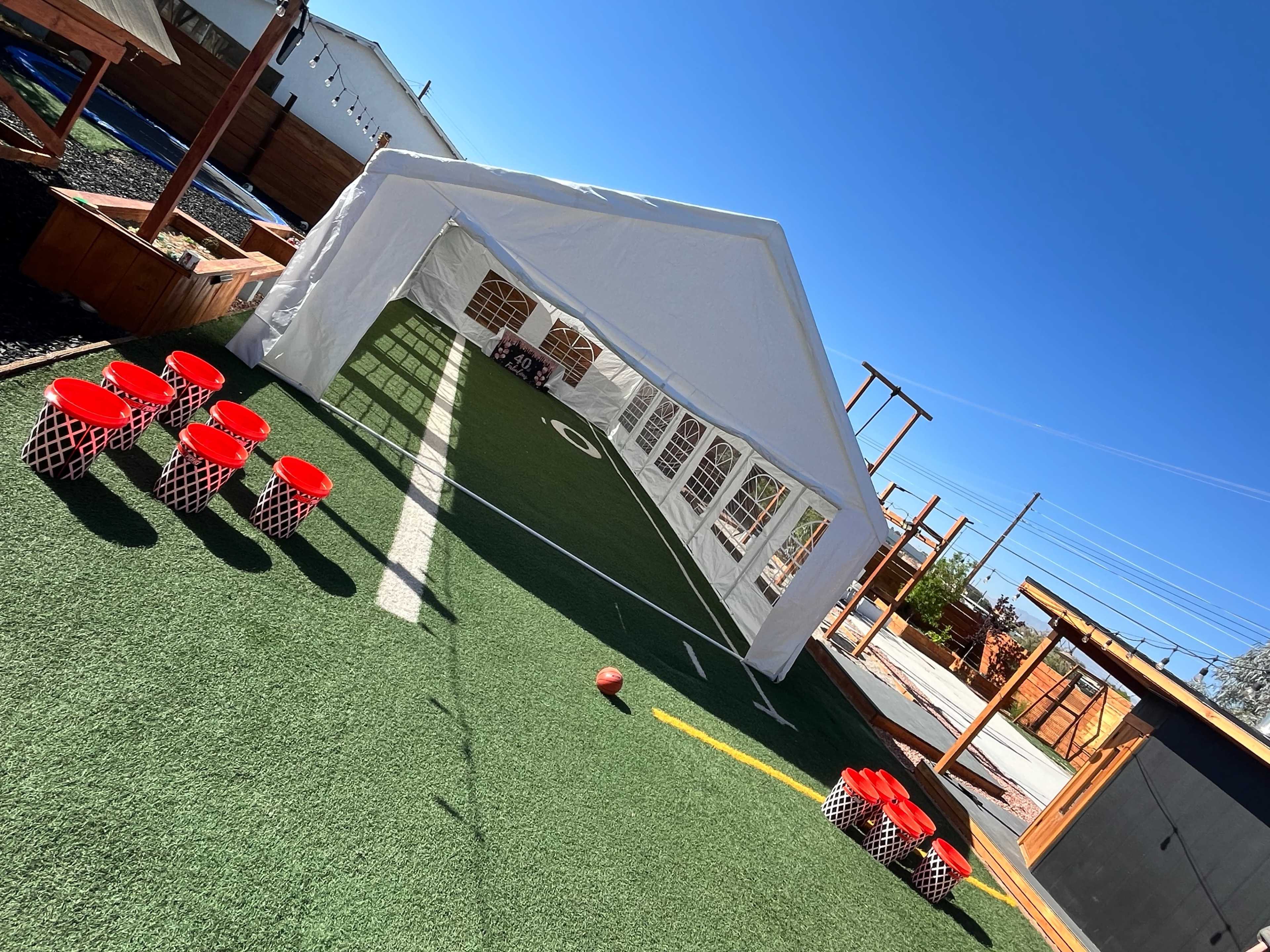 The image shows a white tent set up over a green turf field with red plastic containers arranged on one side.