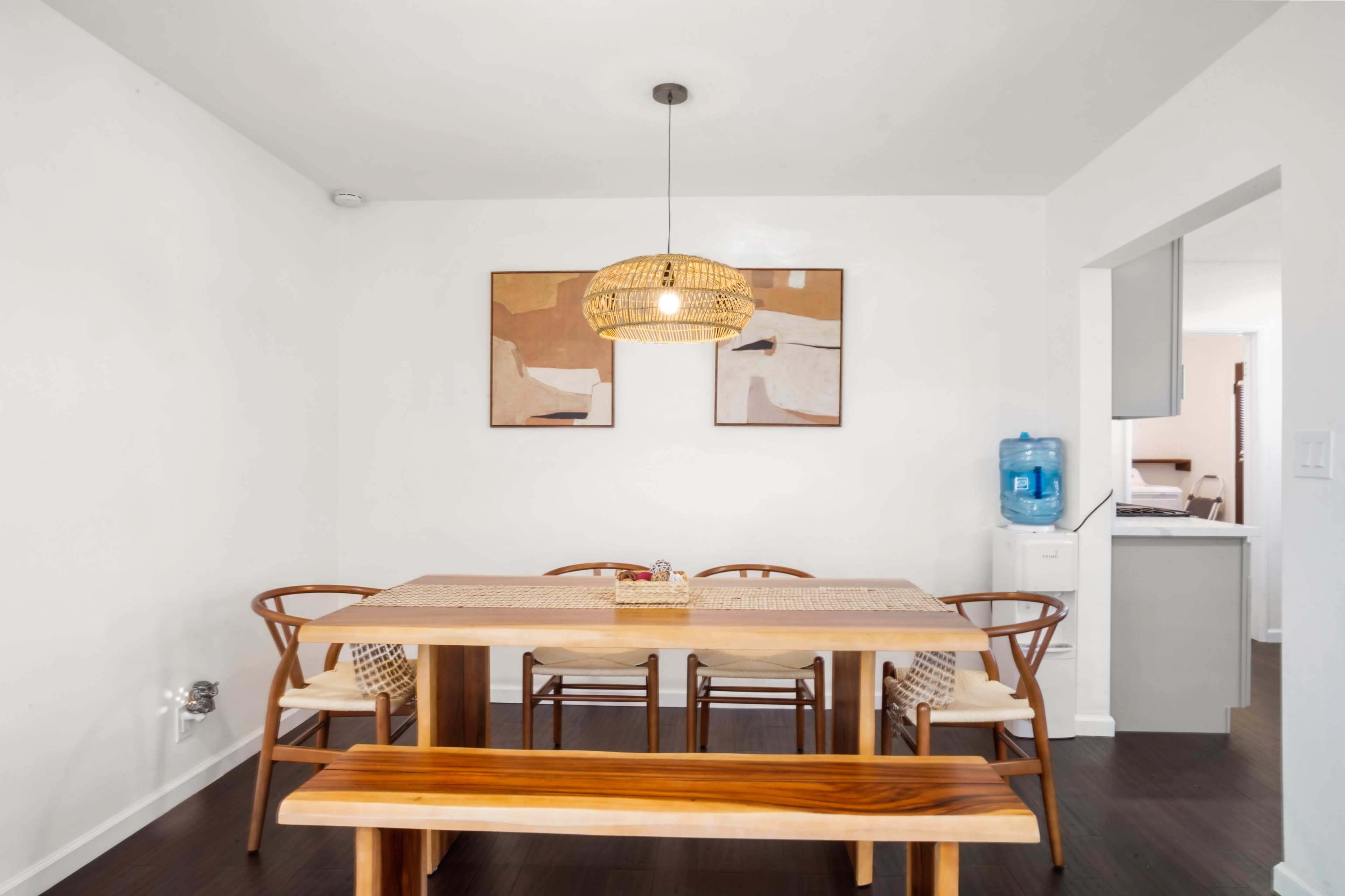 A dining area features a wooden table surrounded by chairs, a pendant light above, and abstract artworks on the wall.