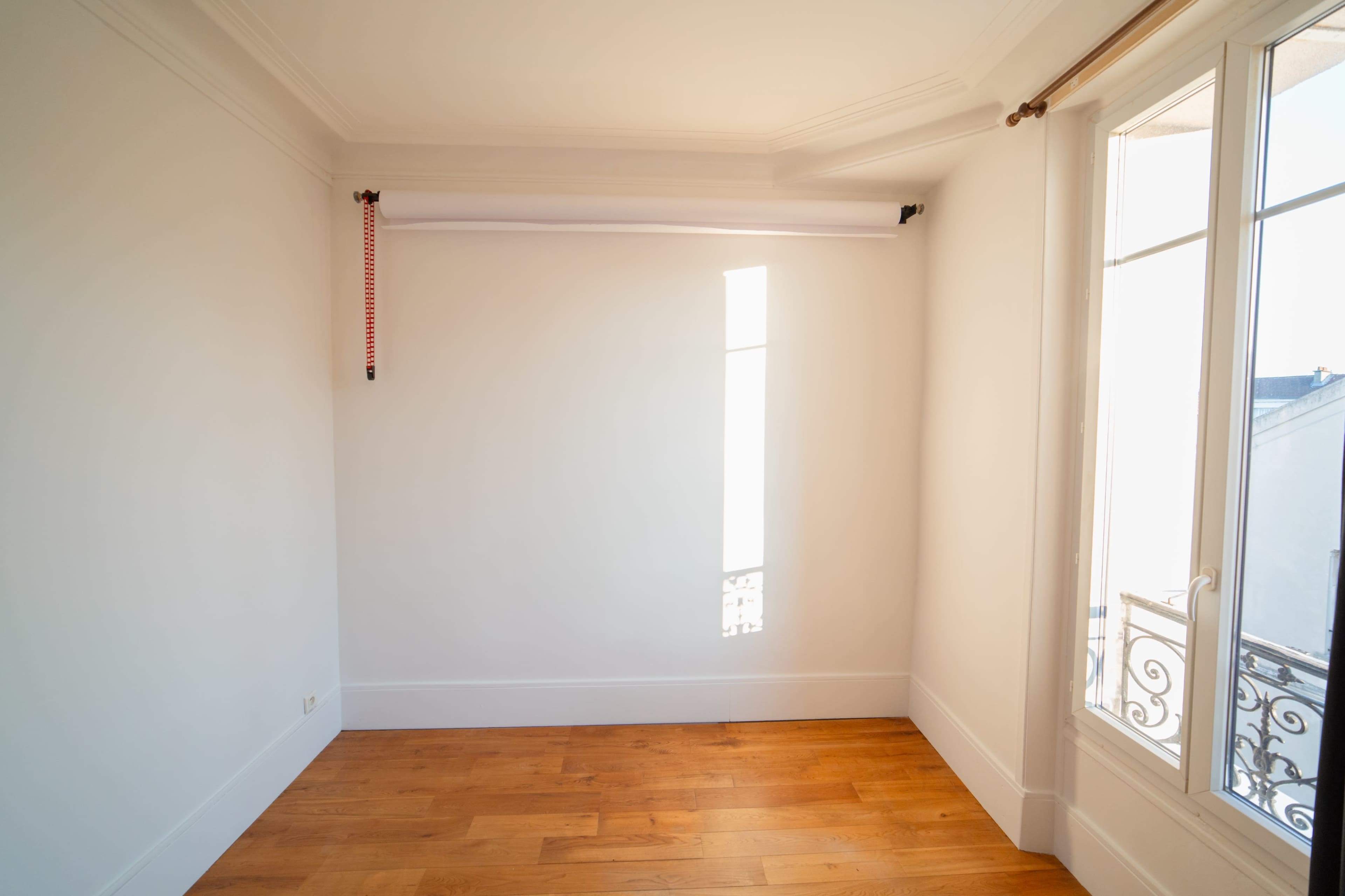 A bright, empty room with wooden flooring and a single window featuring a partially drawn blind.