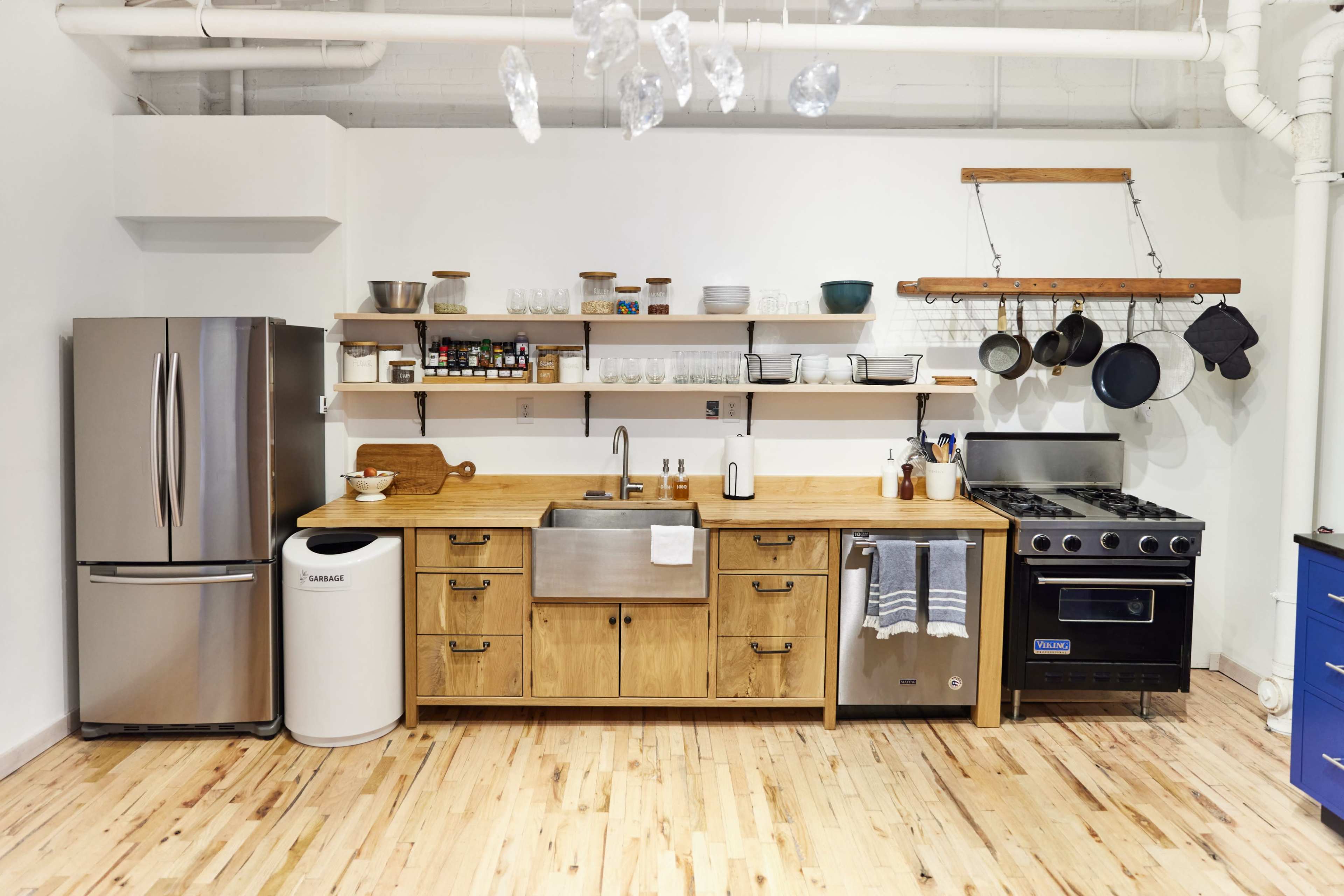 The kitchen features stainless steel appliances, a wooden countertop, open shelving with dishware, and hanging pots.