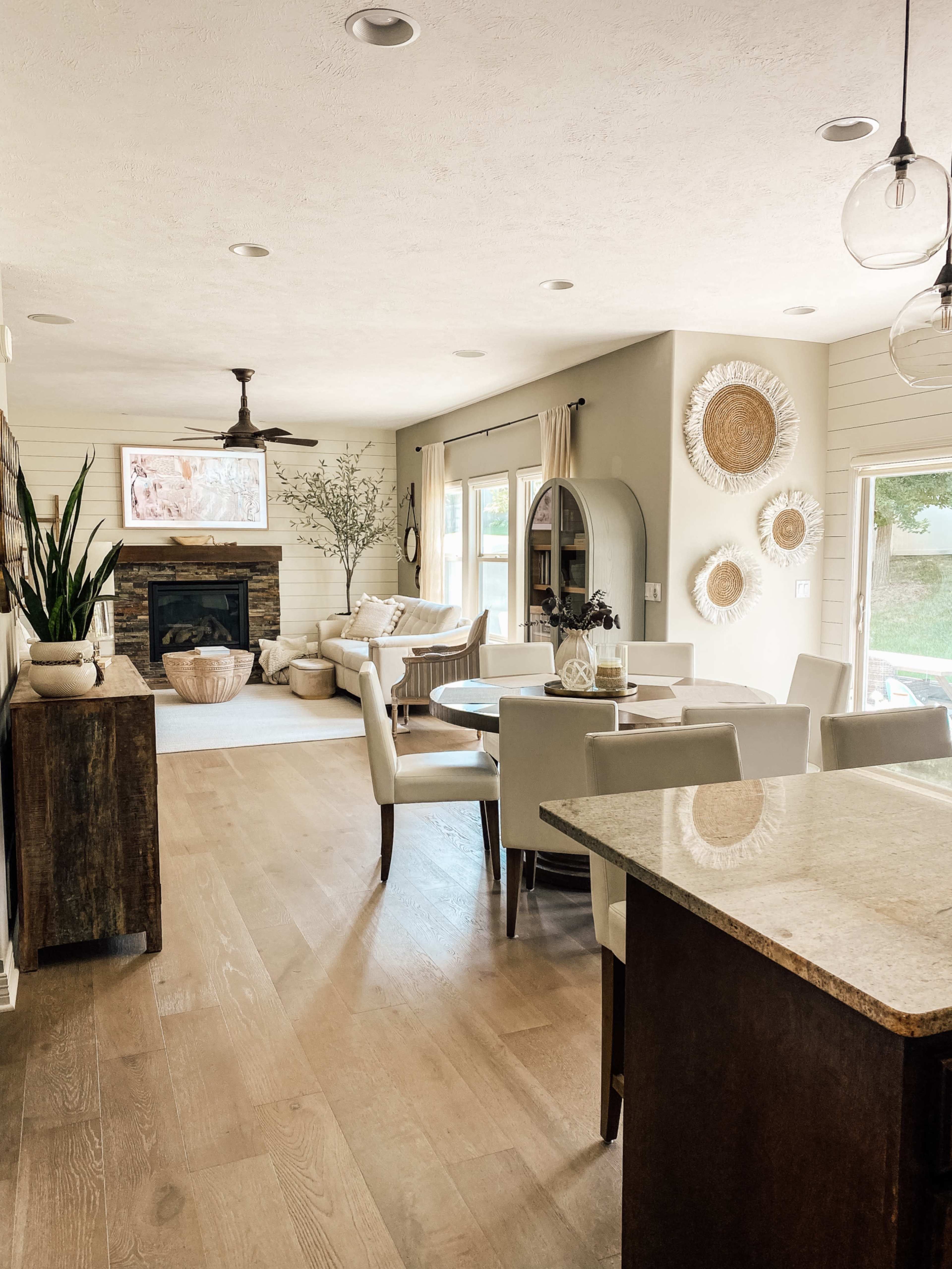 A light-filled living space features a dining area with a wooden table, a cozy seating area with a fireplace, and decorative wall accents.