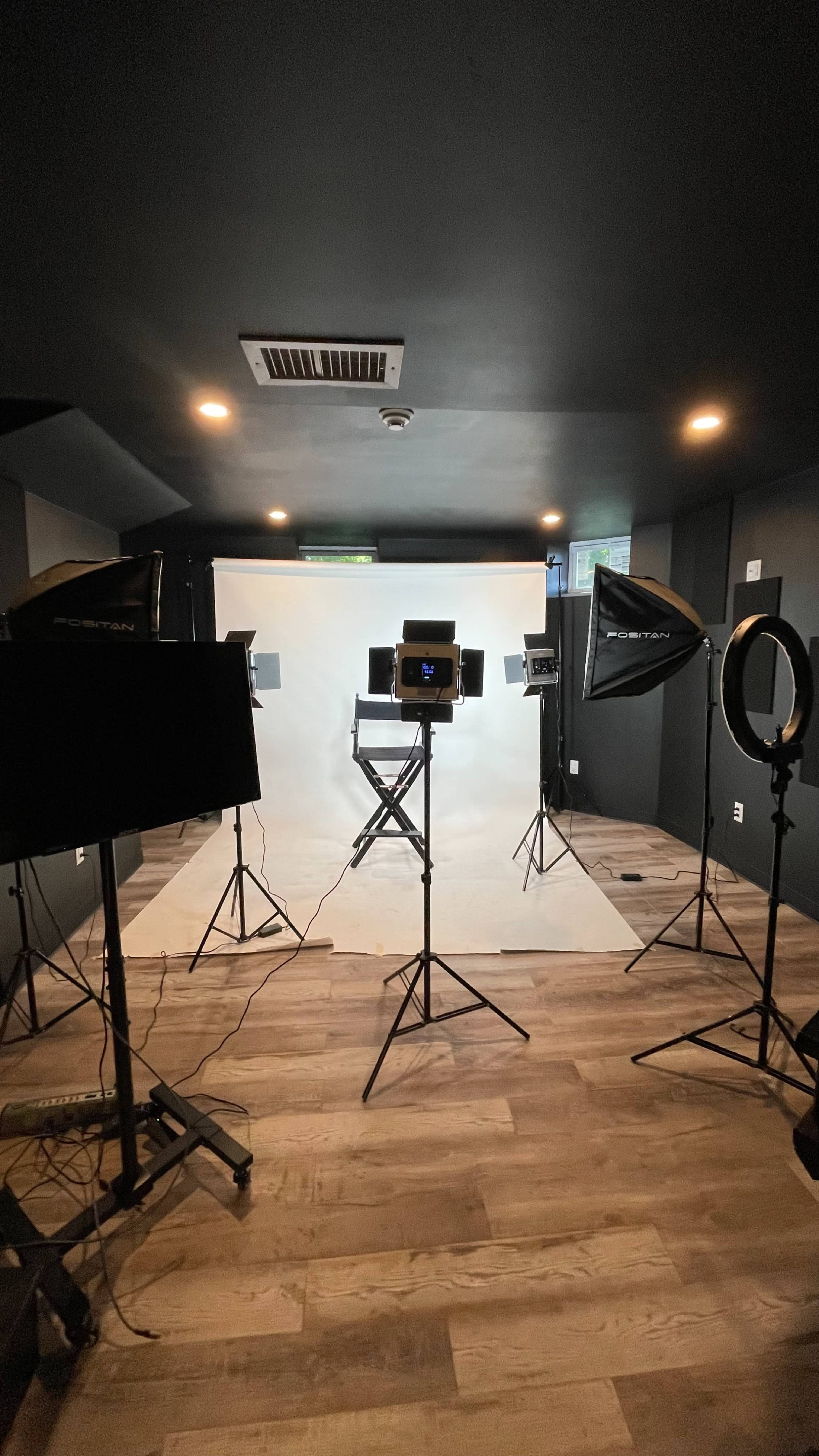 The image shows a photography studio set up with lighting equipment, a white backdrop, and a director's chair.