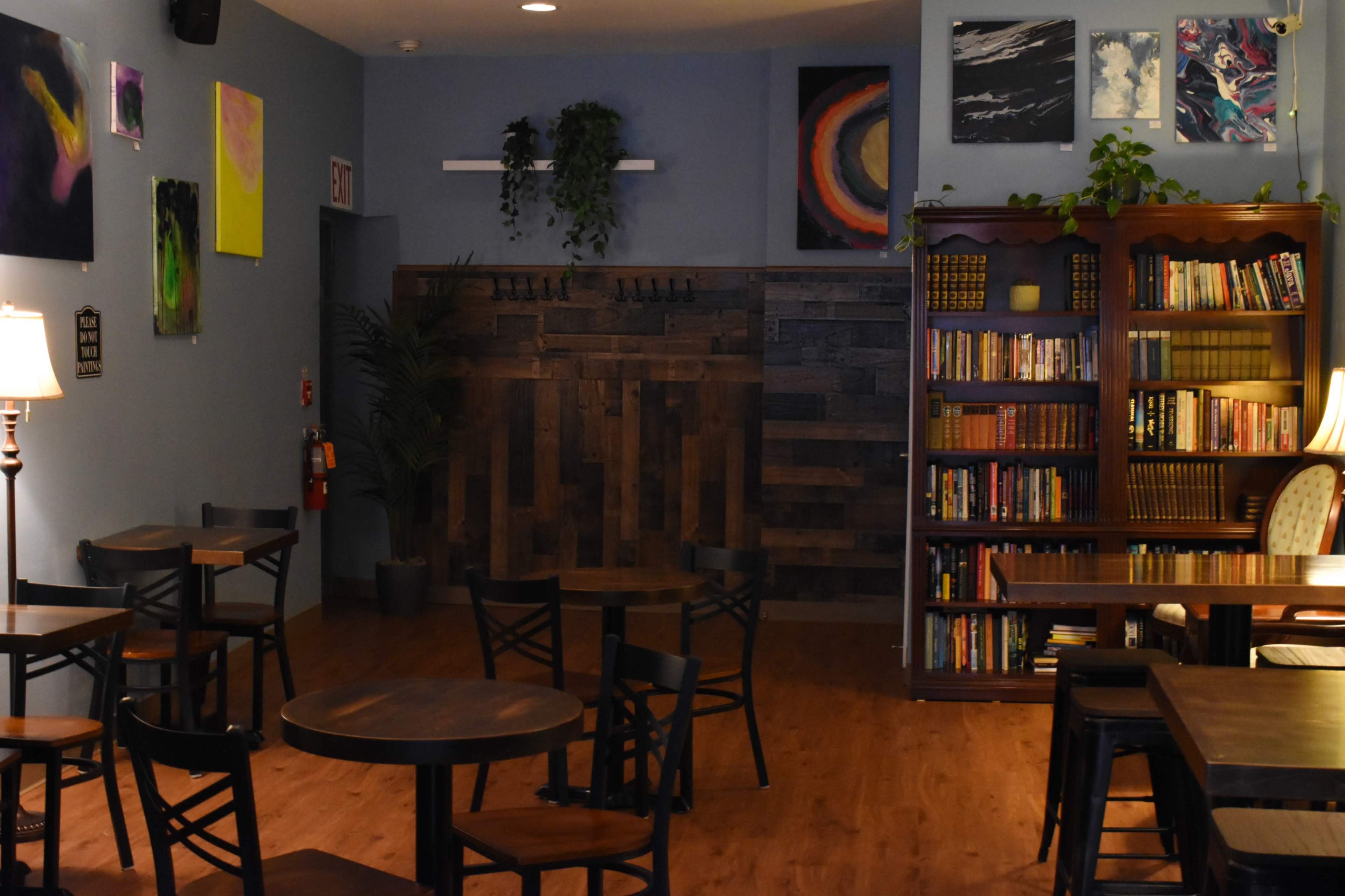 A cozy café interior with wooden tables, a bookshelf filled with books, and colorful artwork displayed on the walls.