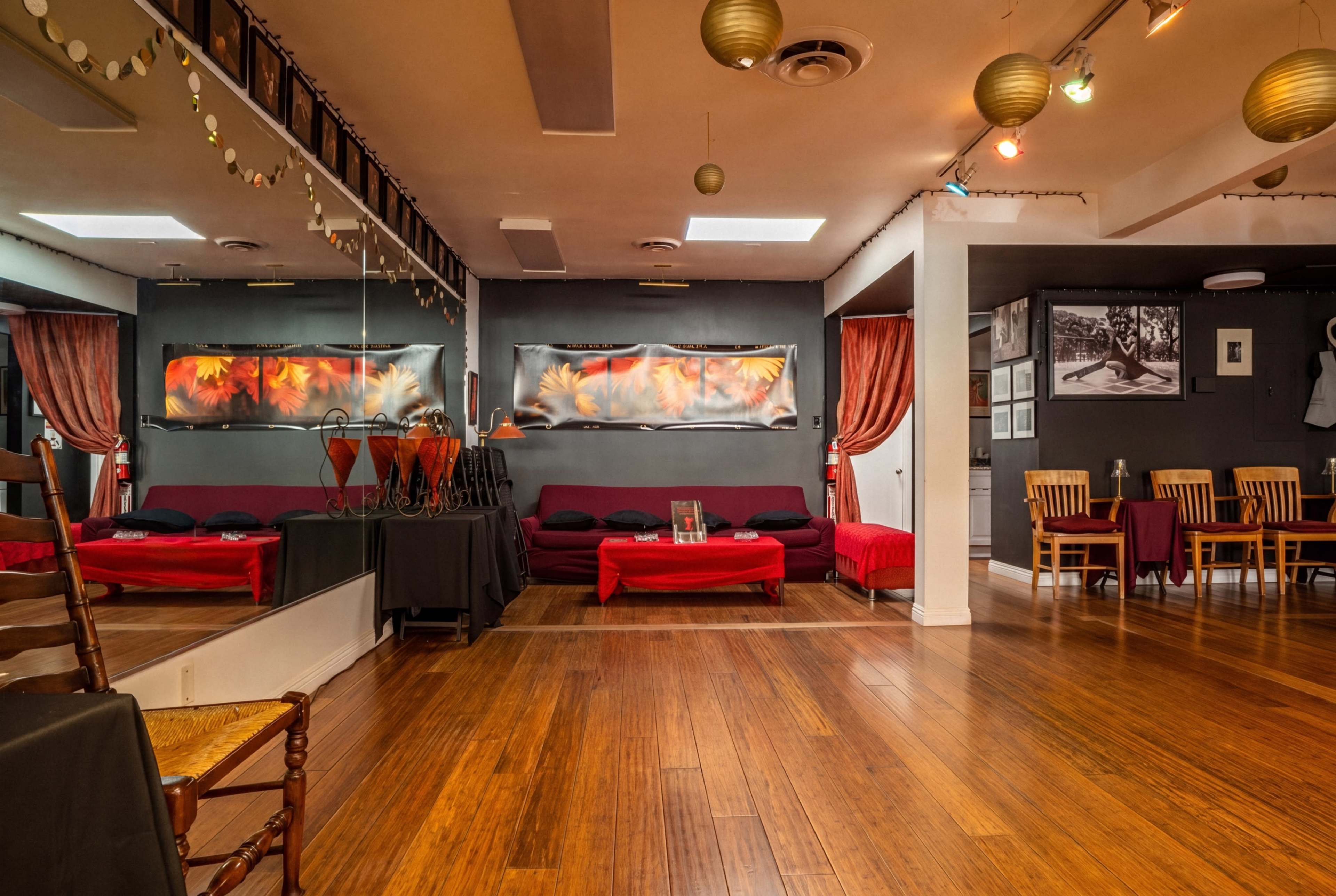 The image depicts a cozy interior space featuring a mirrored wall, red and black seating areas, and wooden tables arranged in a dining setup.