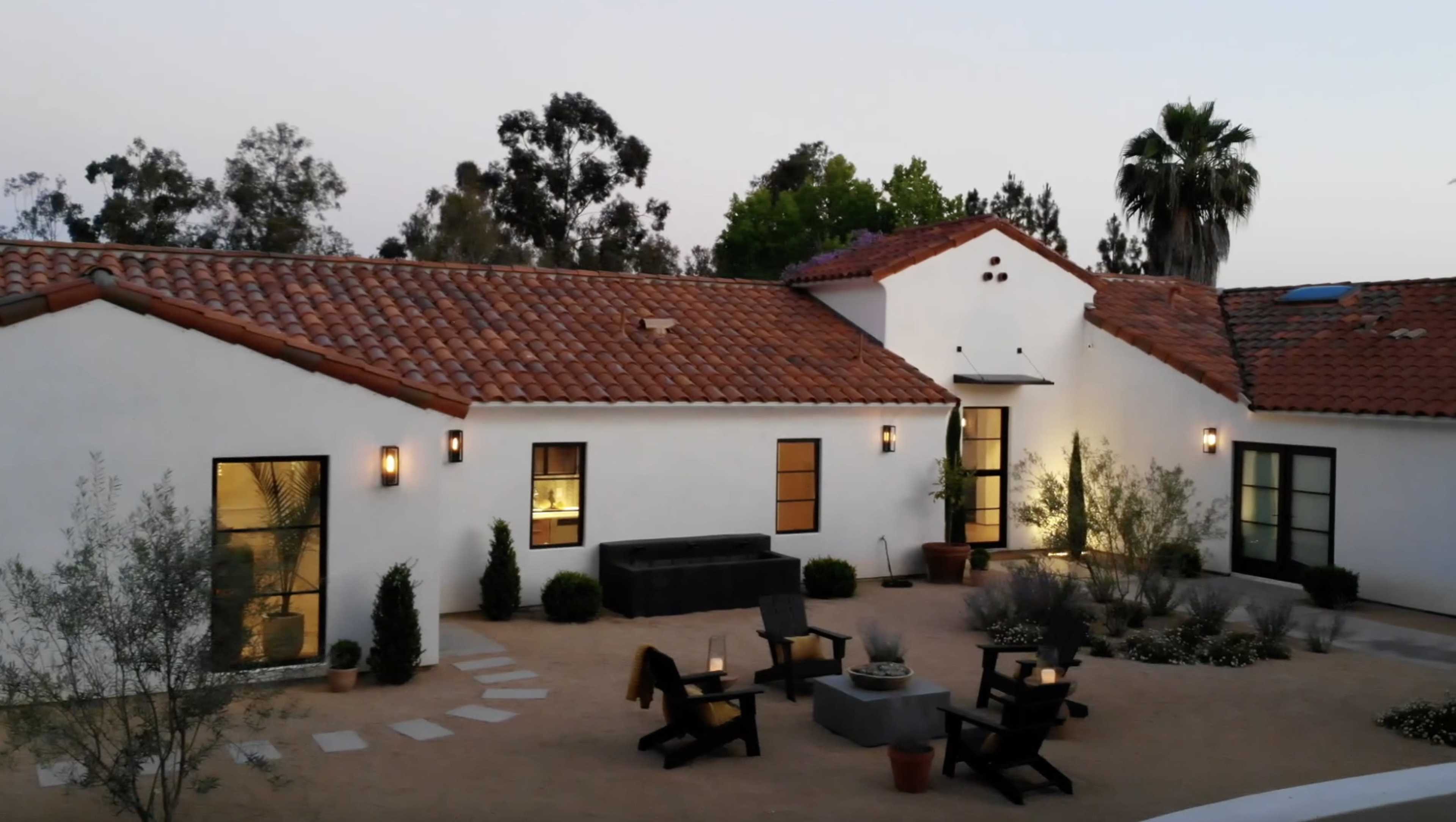 A modern single-story house with a terracotta tile roof, surrounded by a gravel courtyard featuring seating areas and landscaping.