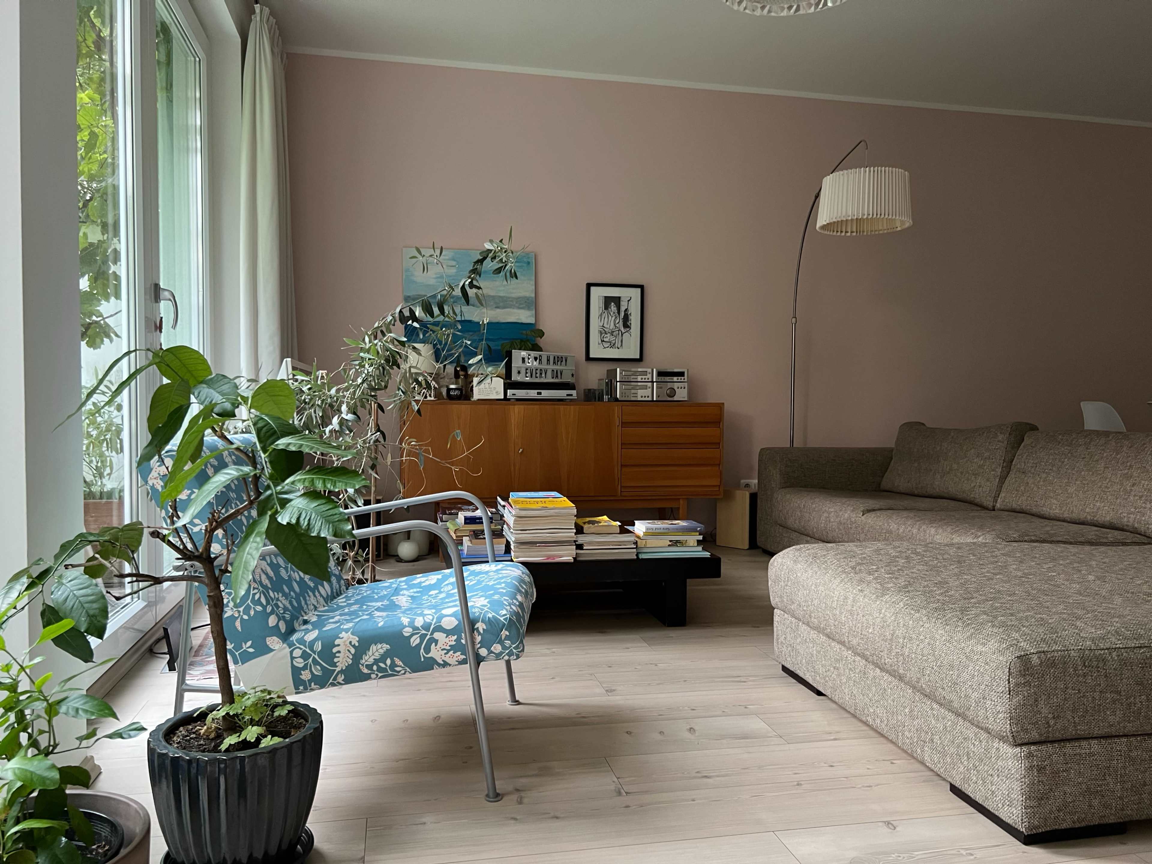 A cozy living room features a large sectional sofa, a small blue chair with a floral pattern, a wooden sideboard, and a plant in a pot near a window.