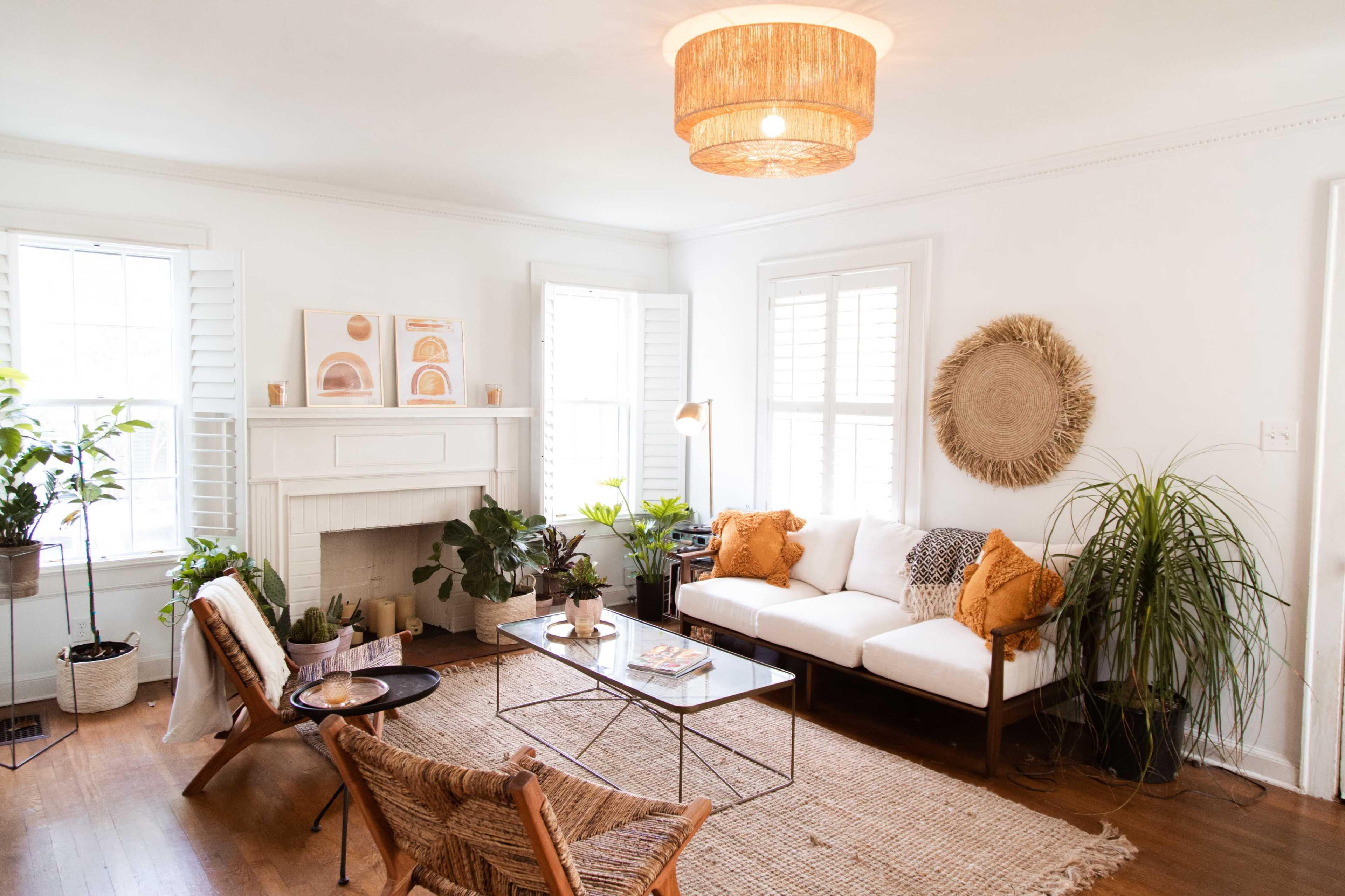 A bright living room featuring a white sofa, plants, a coffee table, and decorative wall art, with natural light streaming through two window openings.