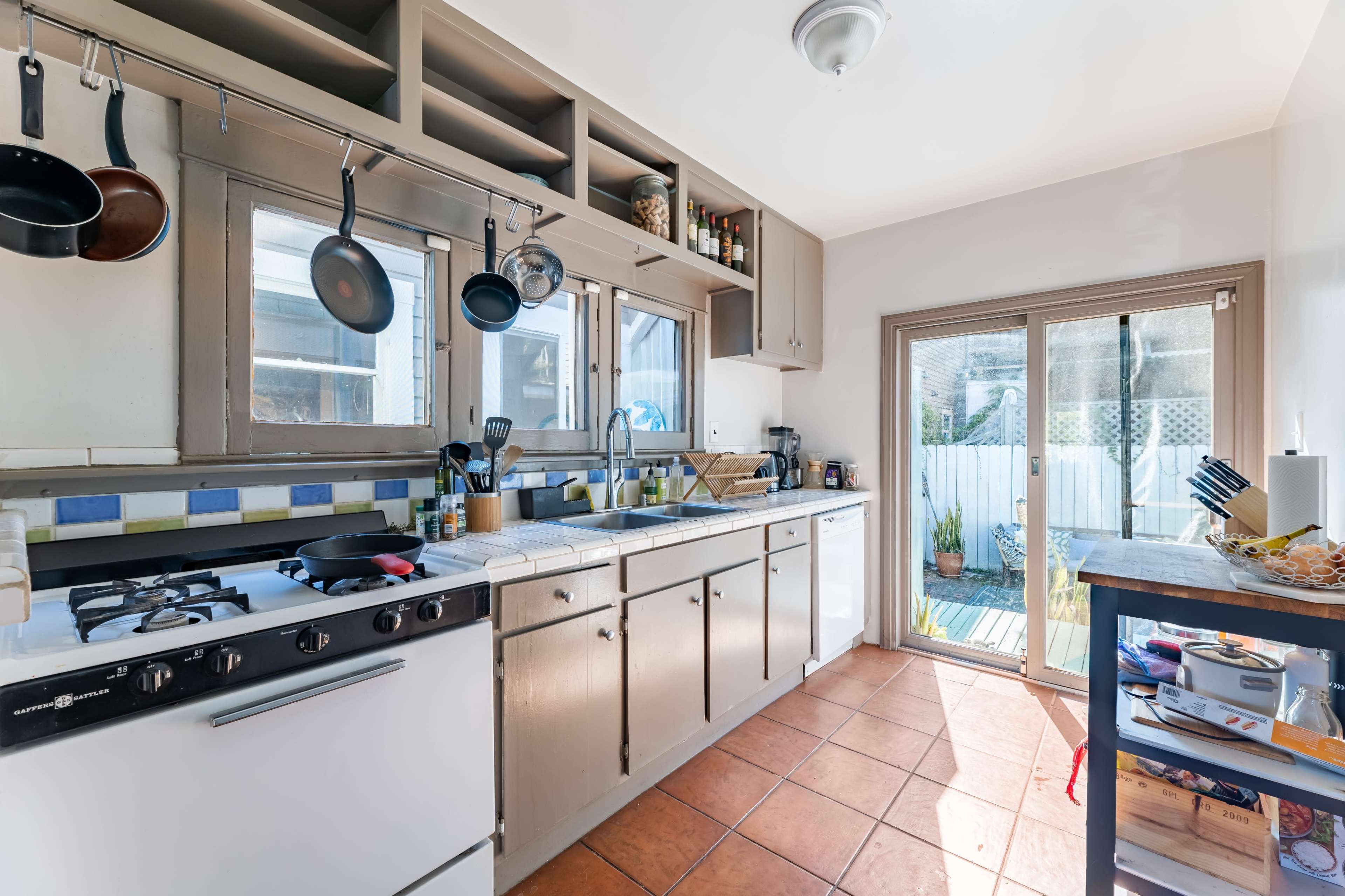 The kitchen features tiled countertops, a gas stove, and a sliding glass door leading to an outdoor area.