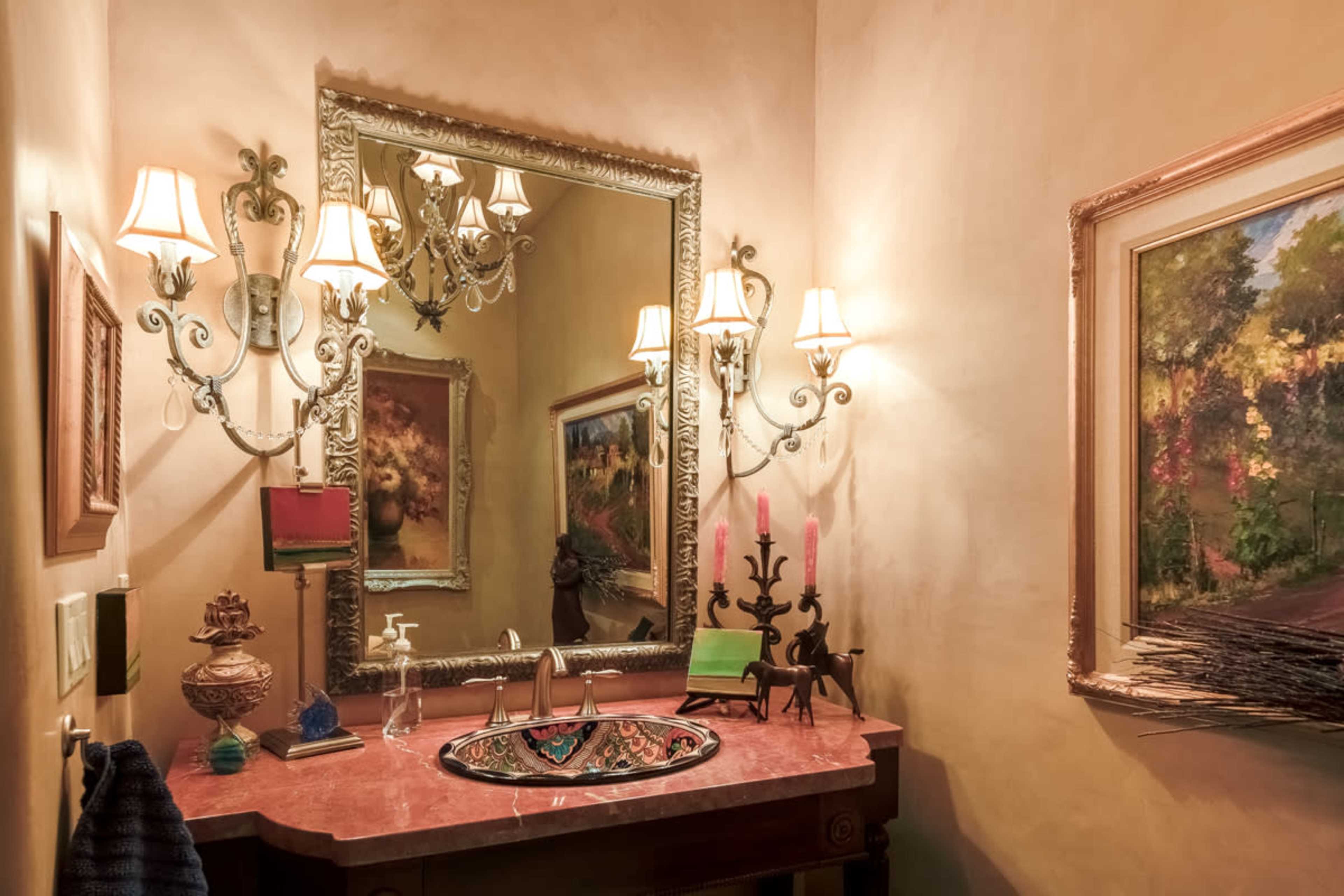 A small bathroom featuring a decorative sink, ornate mirror, wall sconces, and a painting on the wall.