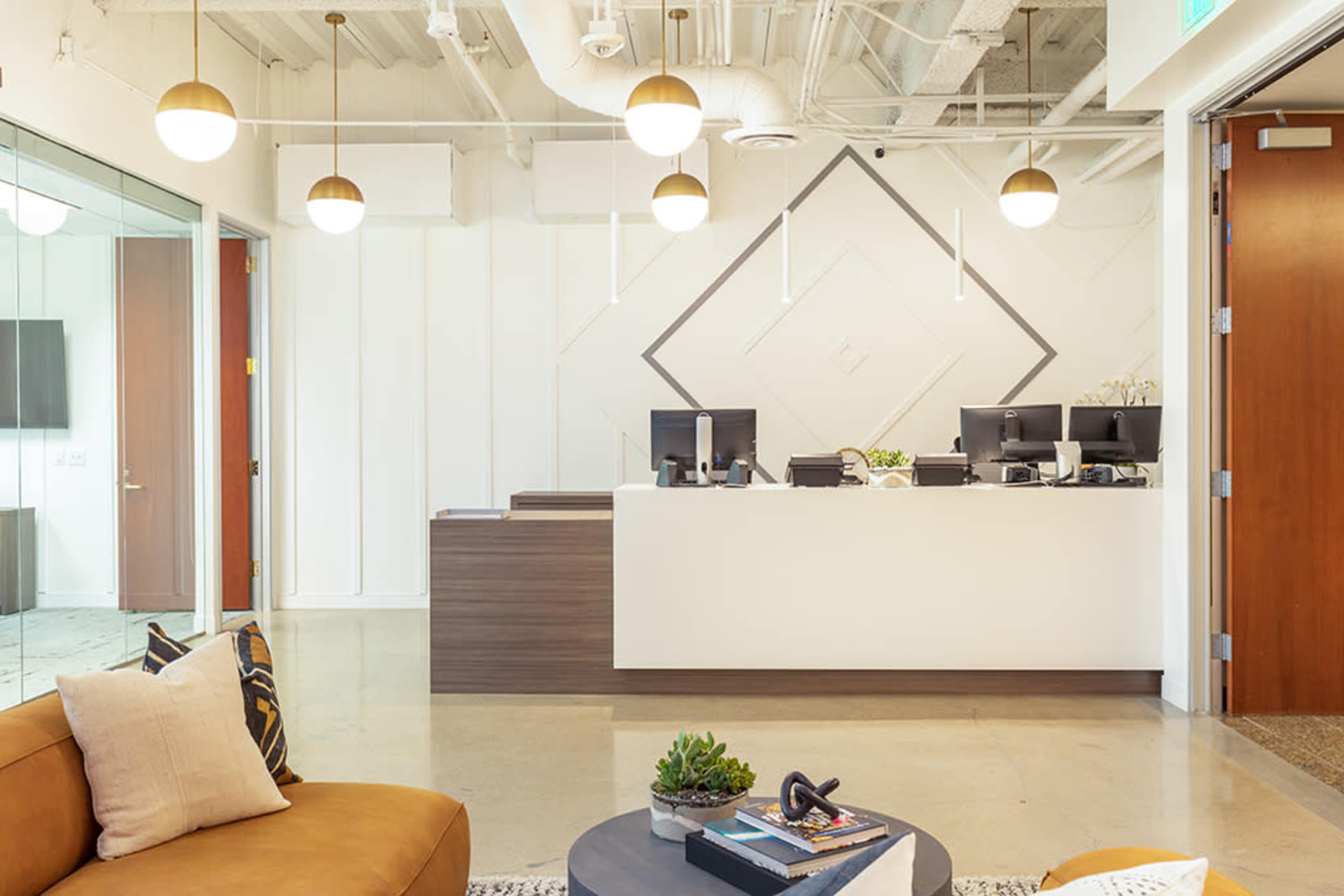 A modern reception area with a white front desk, multiple computer monitors, and a seating area featuring an orange couch and decorative coffee table.