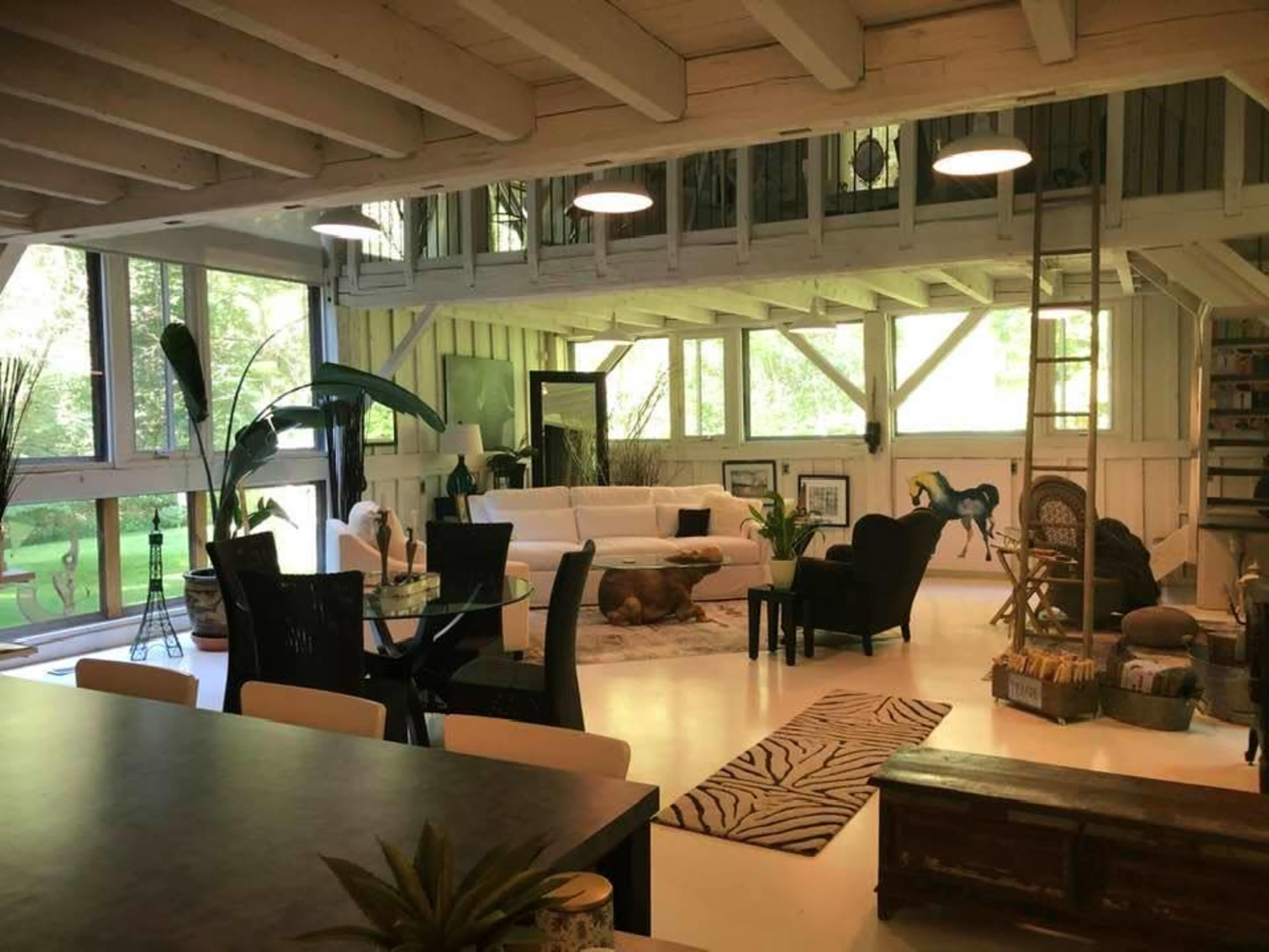 A well-lit, open-concept living space featuring a white sectional sofa, a dining area with a glass table, and large windows overlooking a green landscape.