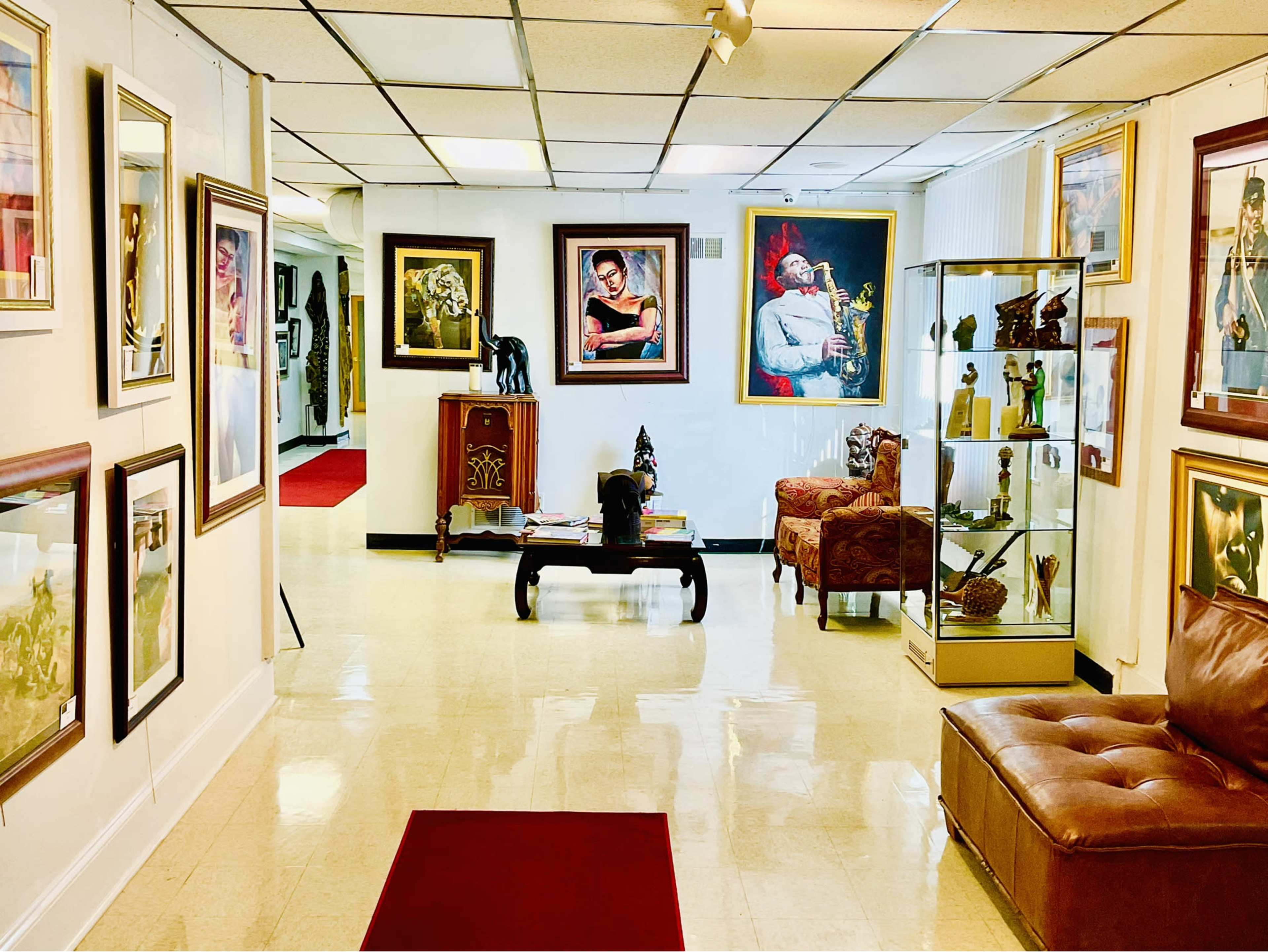 An art gallery with framed paintings and sculptures displayed on the walls and a brown leather couch in the foreground.