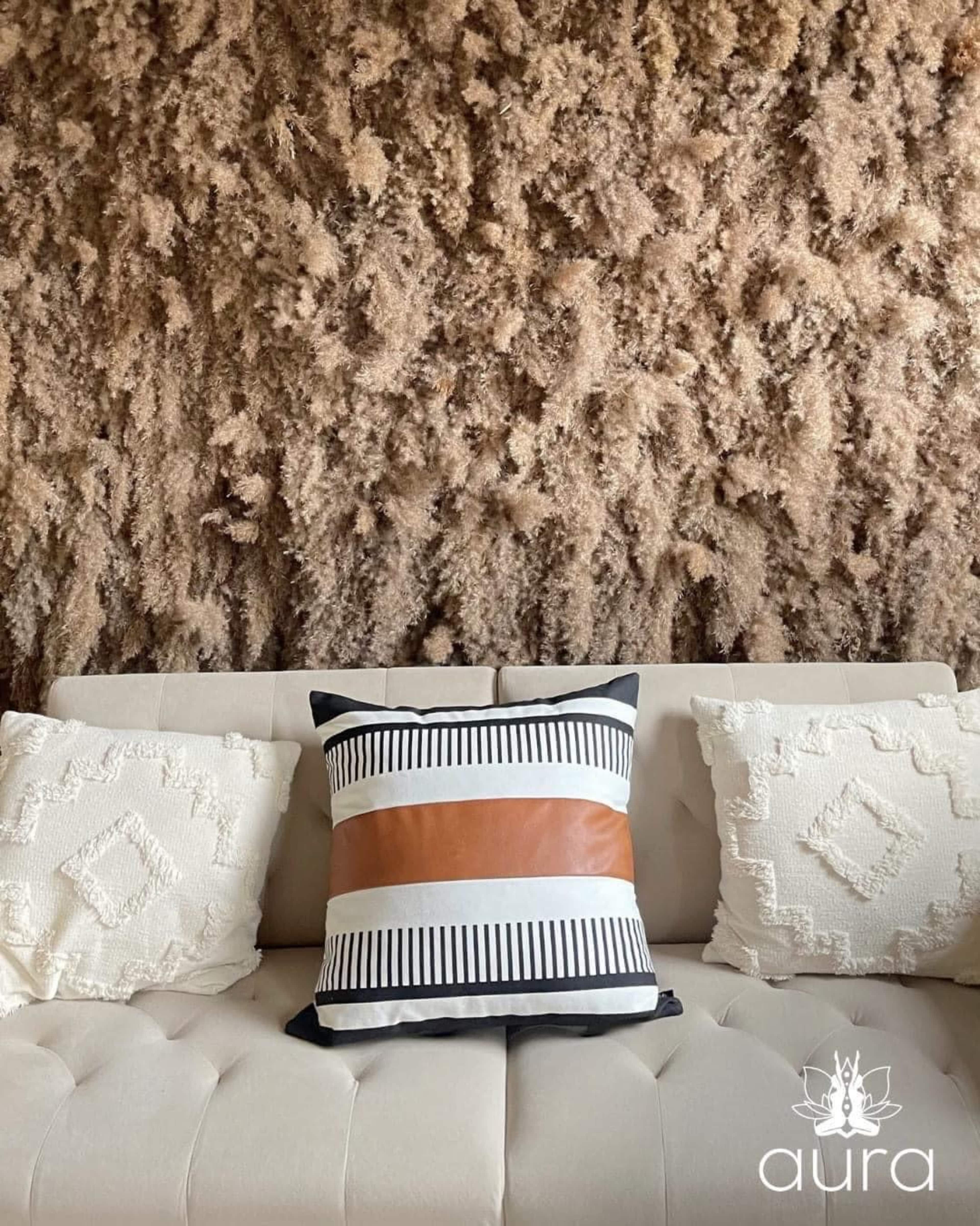 A light-colored sofa is adorned with two decorative pillows and positioned against a textured, earthy wall.