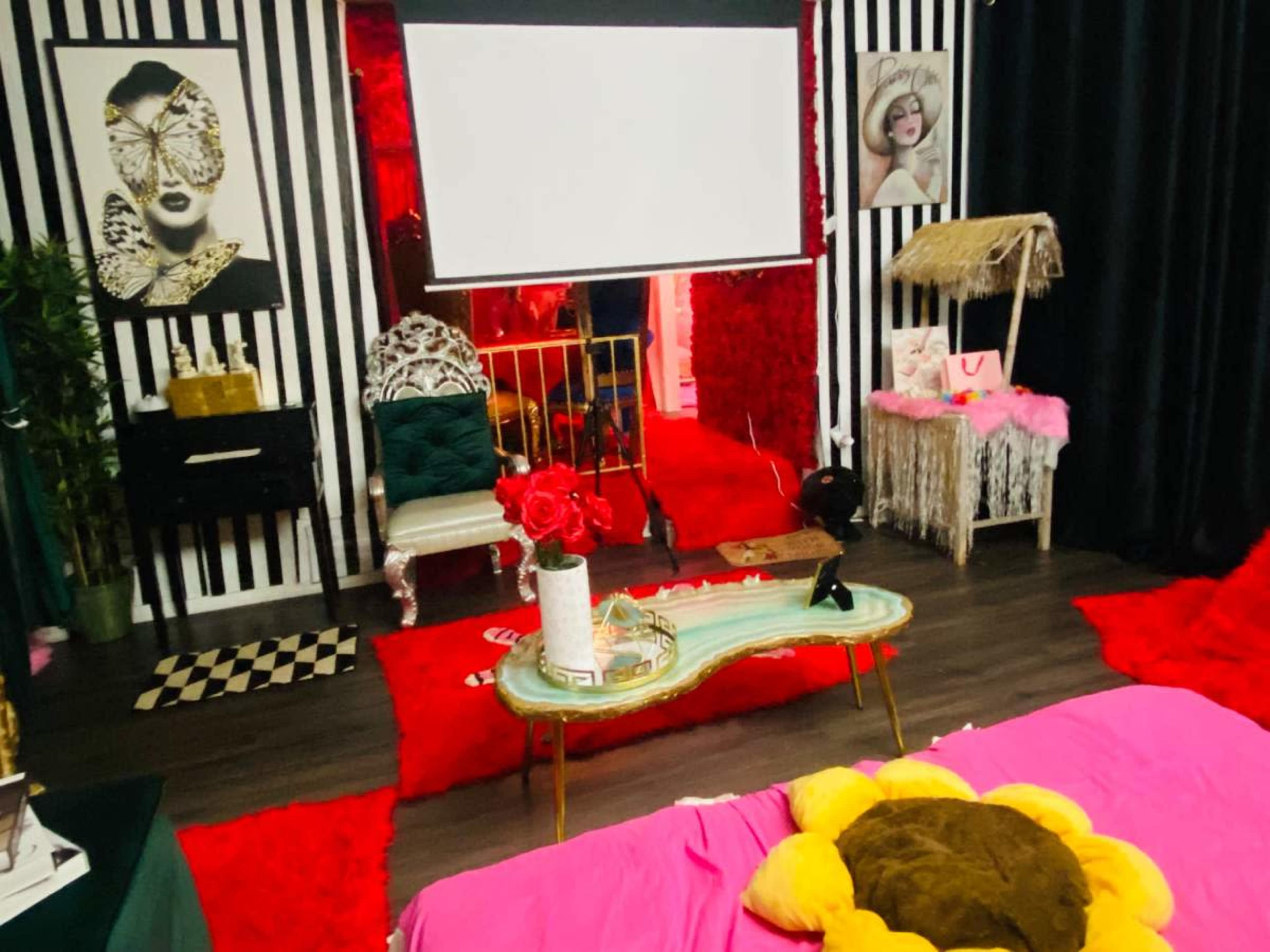 The room features a combination of bold red decor, black and white striped walls, and eclectic furniture, including a large screen and plush seating.