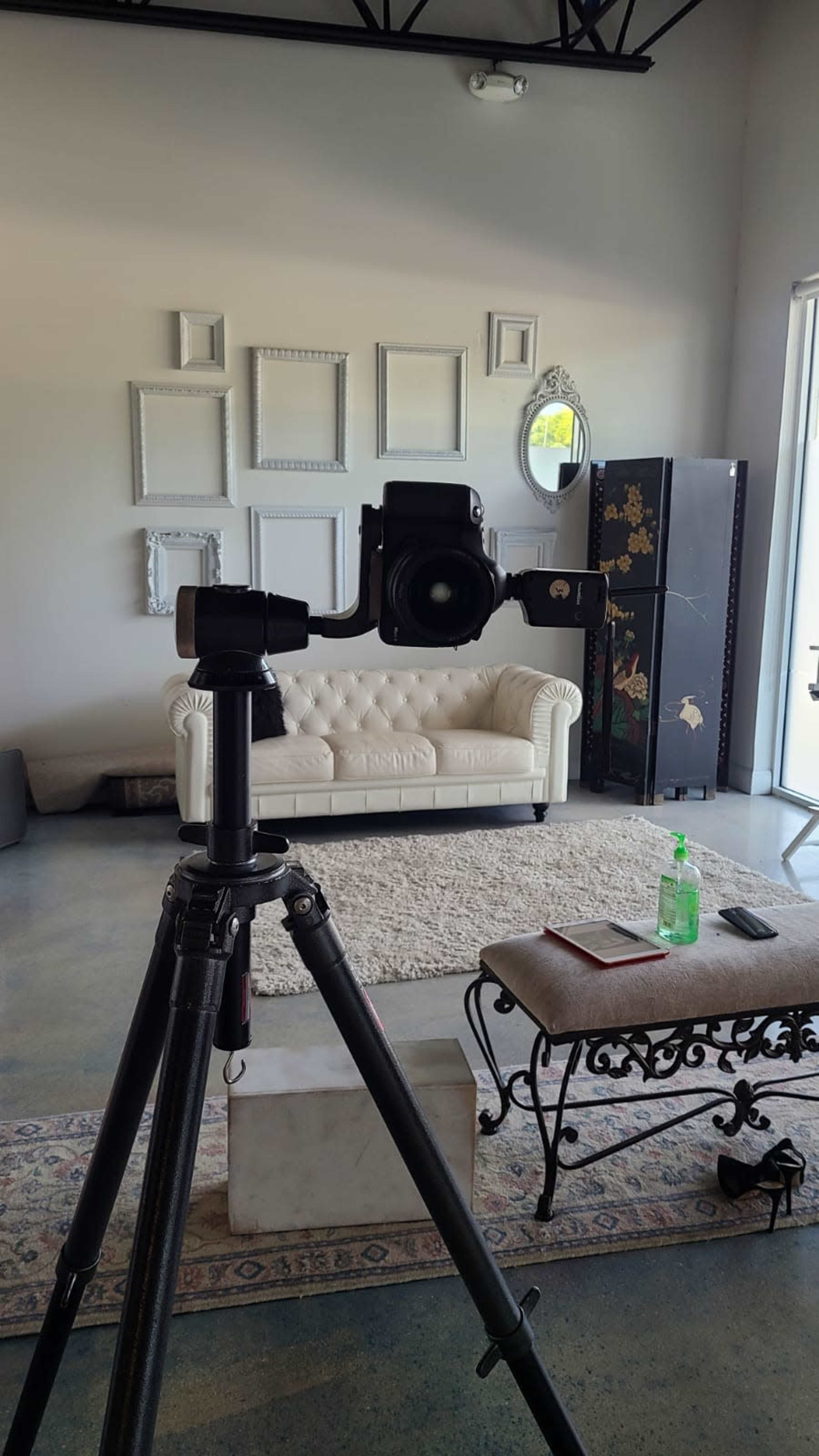 A camera on a tripod is positioned in front of a white couch and decorative wall art in a modern living space.