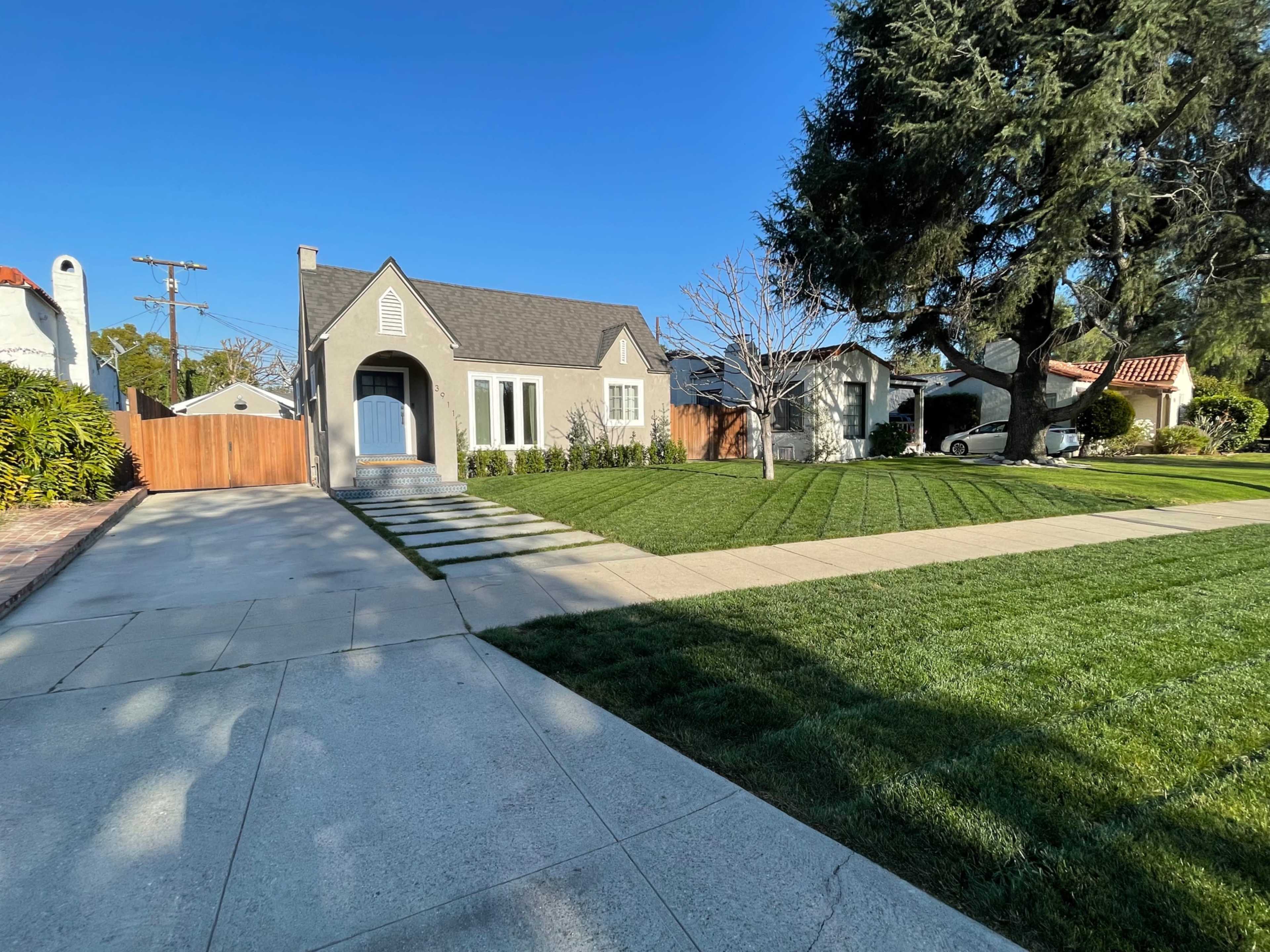The image shows a residential area with a gray house, neatly manicured grass, and a clear blue sky.