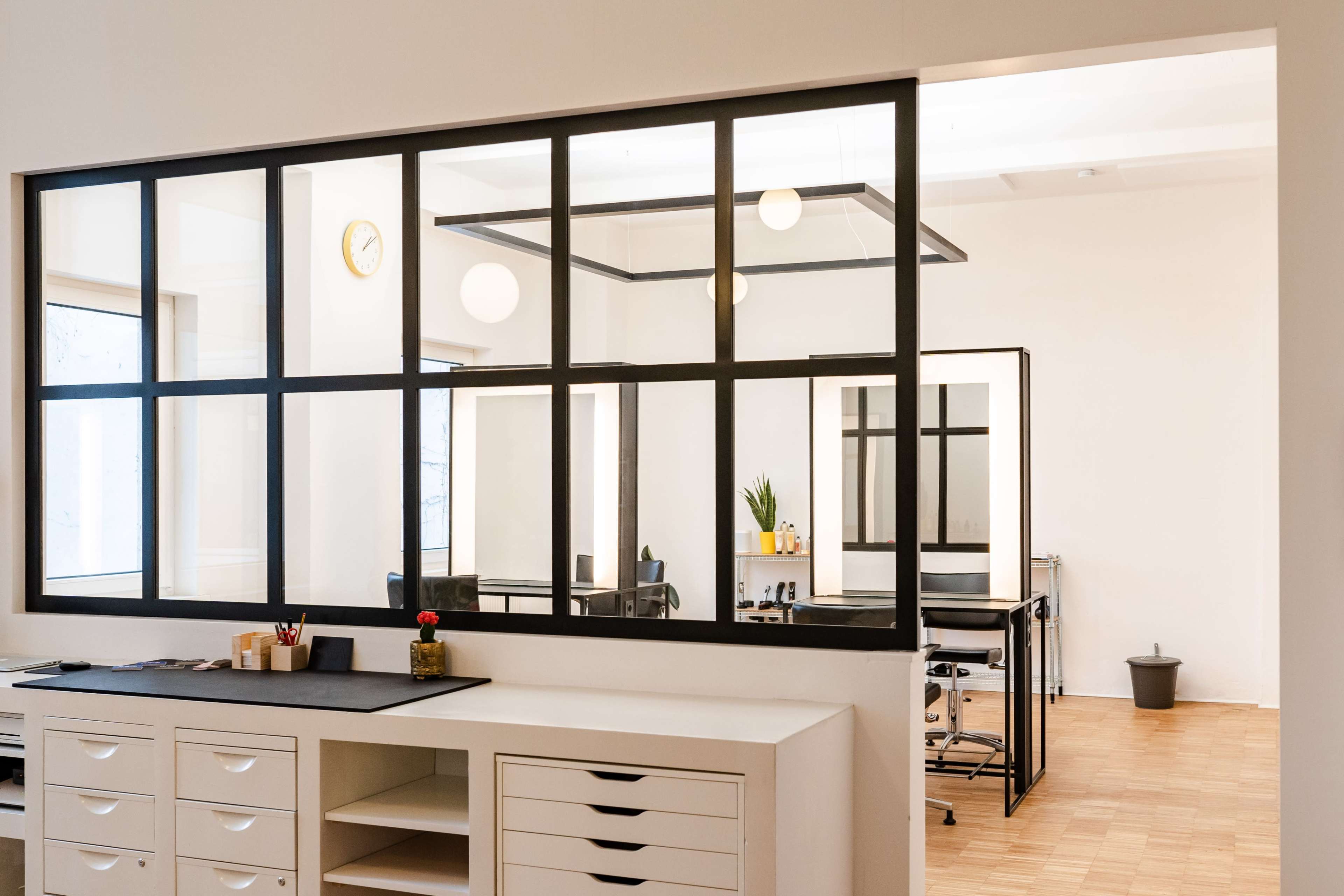 A modern office space divided by a large glass window with a minimalistic design and neutral colors.