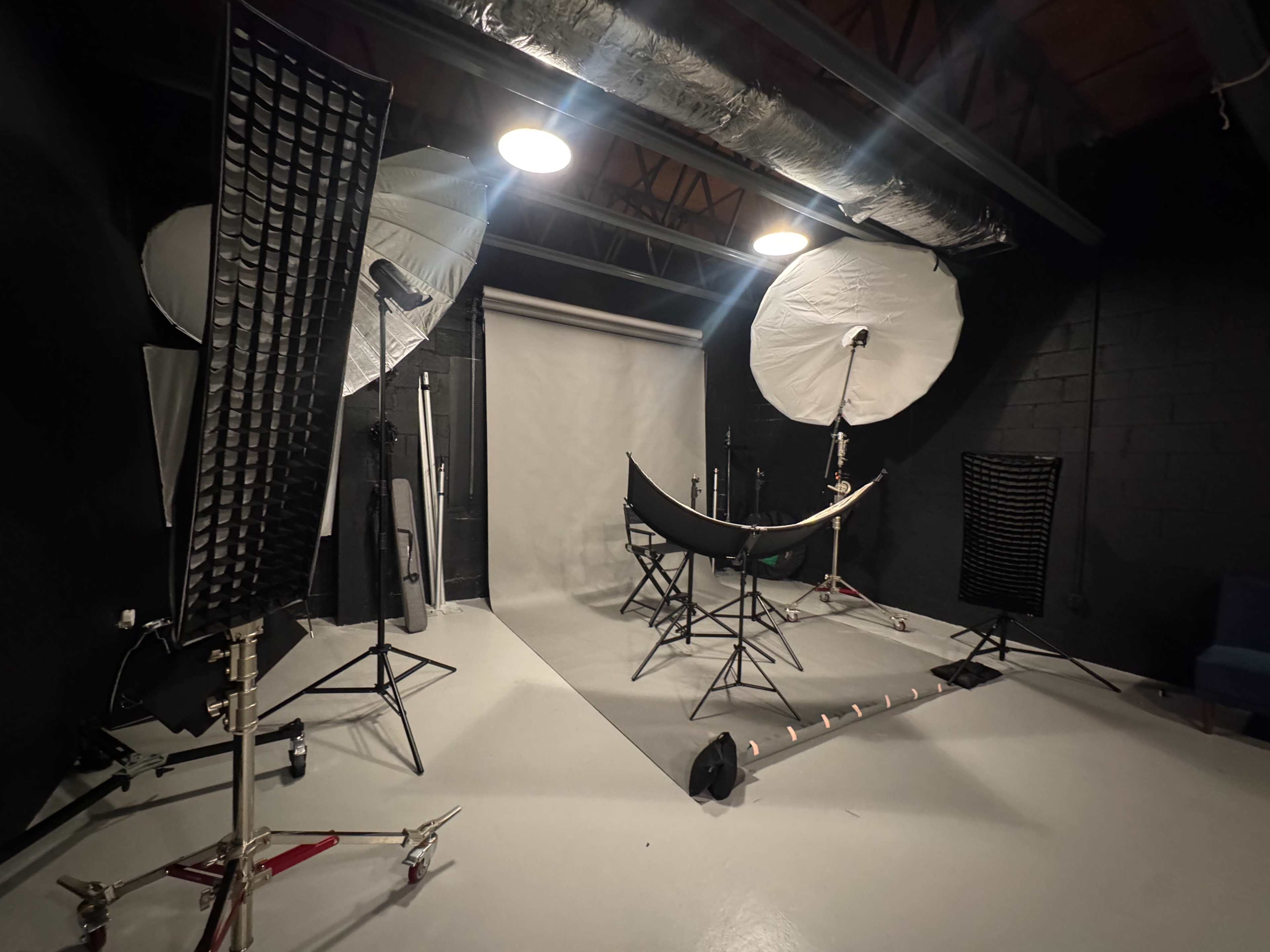 The image shows a photography studio equipped with softbox lights, a backdrop, and various lighting stands arranged around a central area with a hammock and chairs.