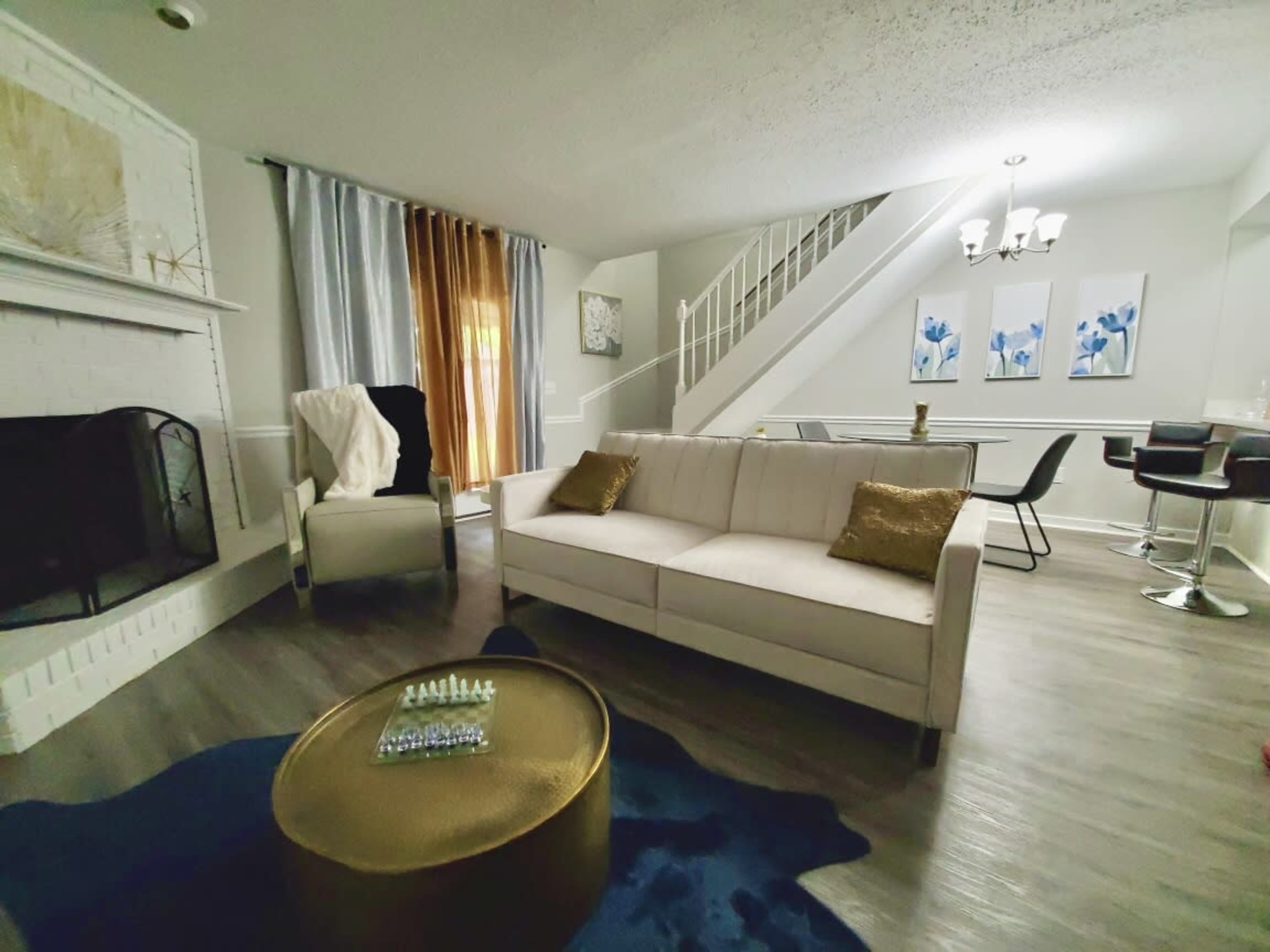 A modern living room features a beige sofa, a gold coffee table, and a staircase in the background.