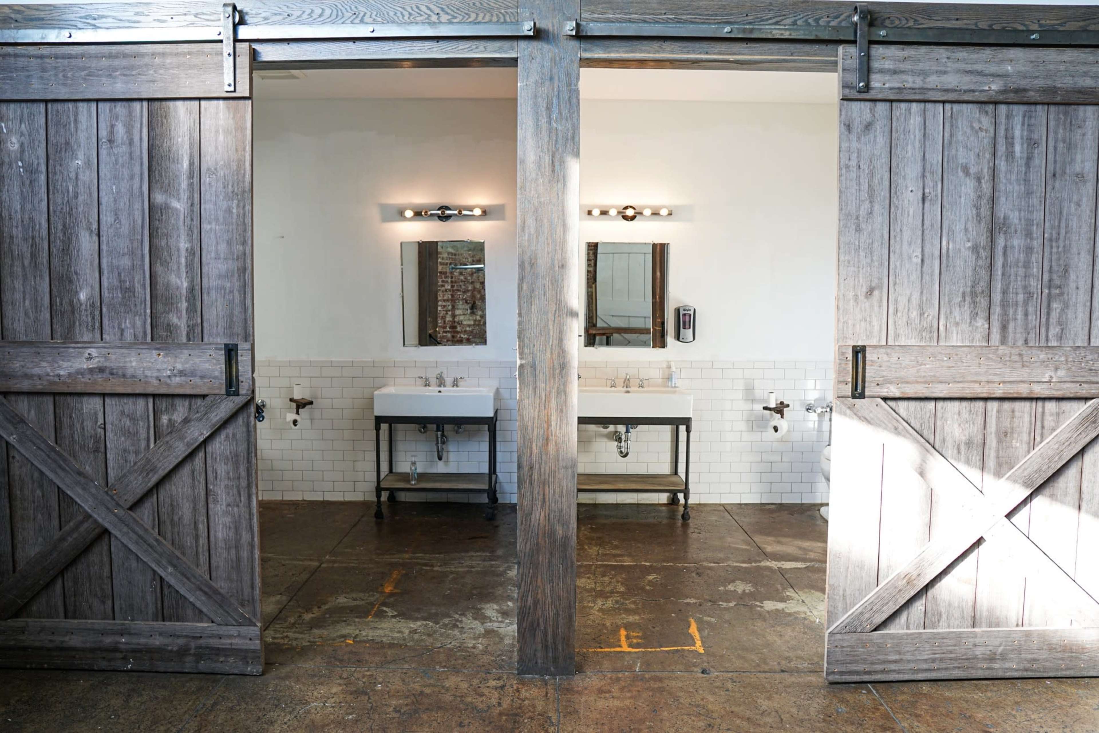 A rustic-style restroom with two sinks and mirrors, framed by sliding barn doors.