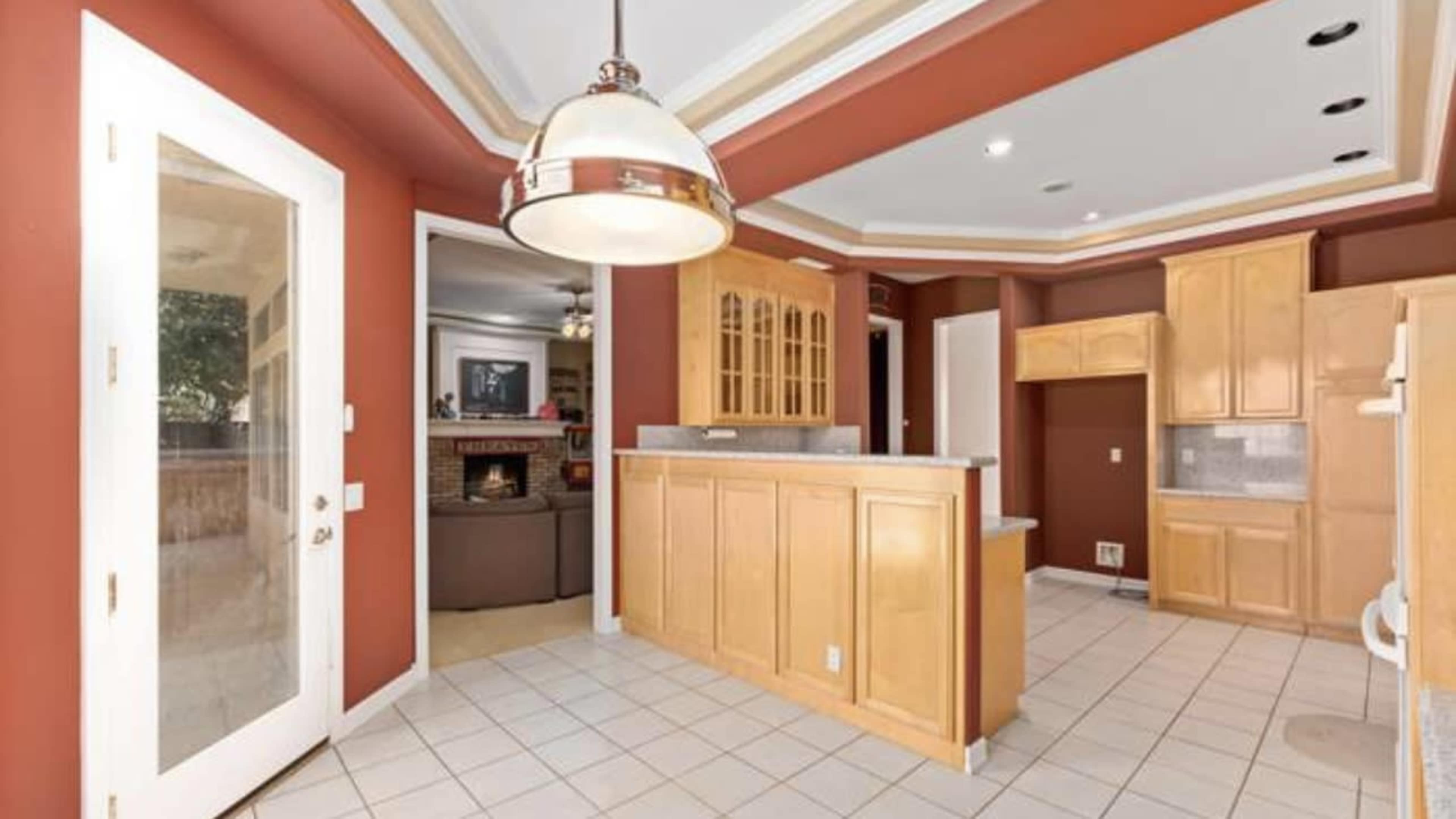 A kitchen with wooden cabinetry, tiled flooring, and a doorway leading to another room with a fireplace.